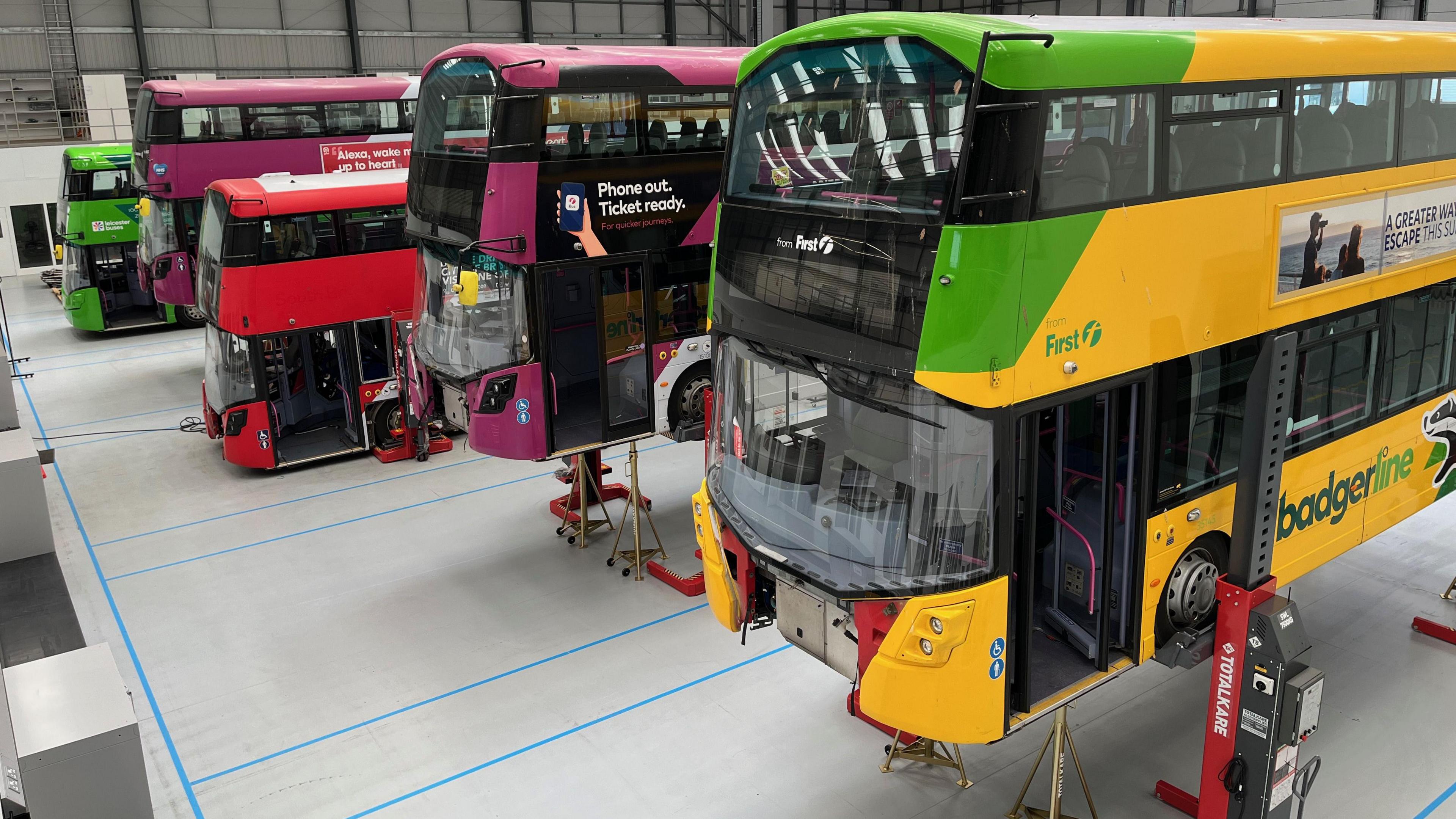 Buses of different colours inside a warehouse