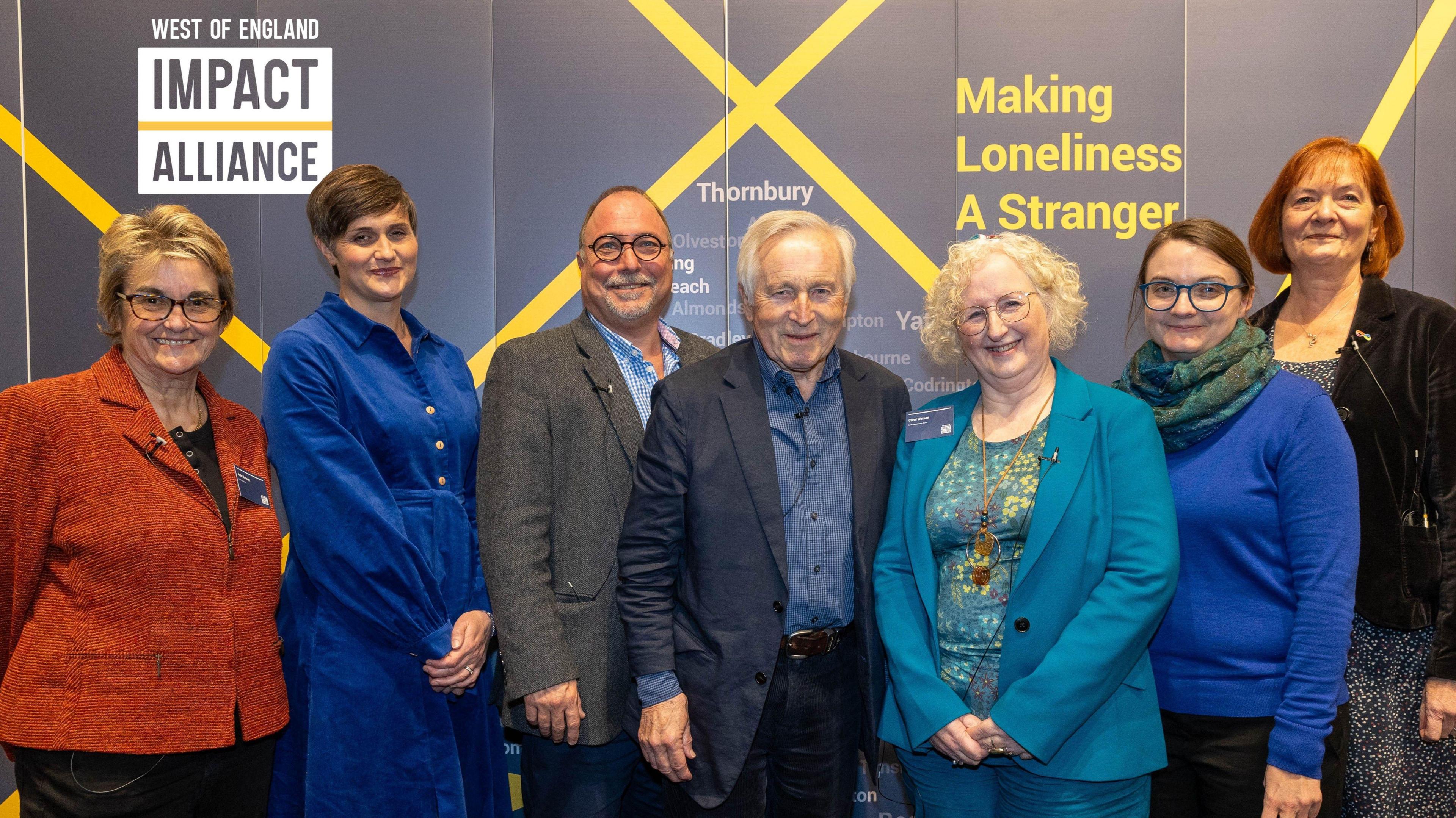 A group of people stand facing the camera at the Bristol Beacon during the launch of the Impact Alliance, a campaign against loneliness. Five of them are women and two are men and they are all smartly dressed