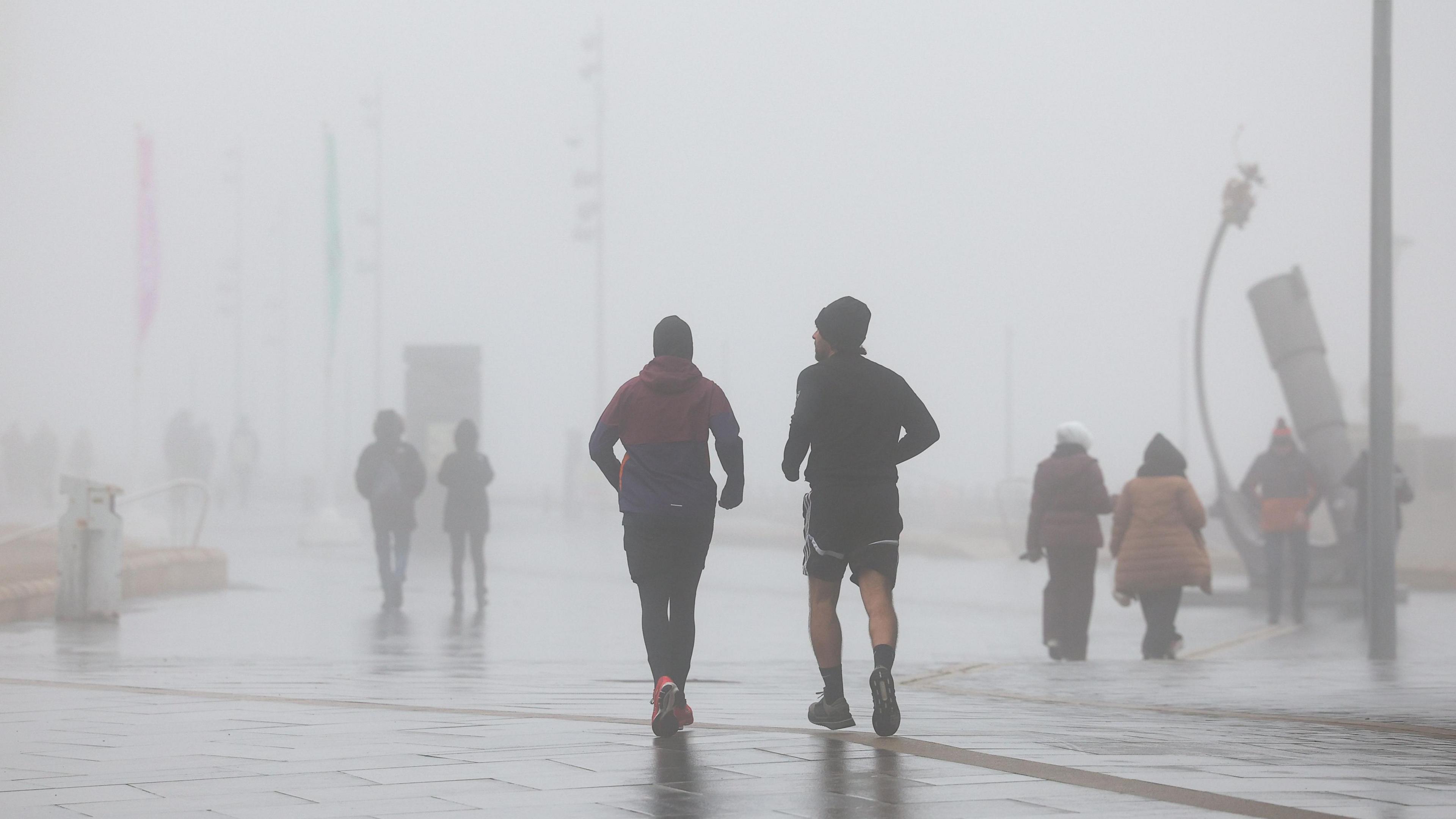 Joggers run through thick fog at the Pier Head in Liverpool