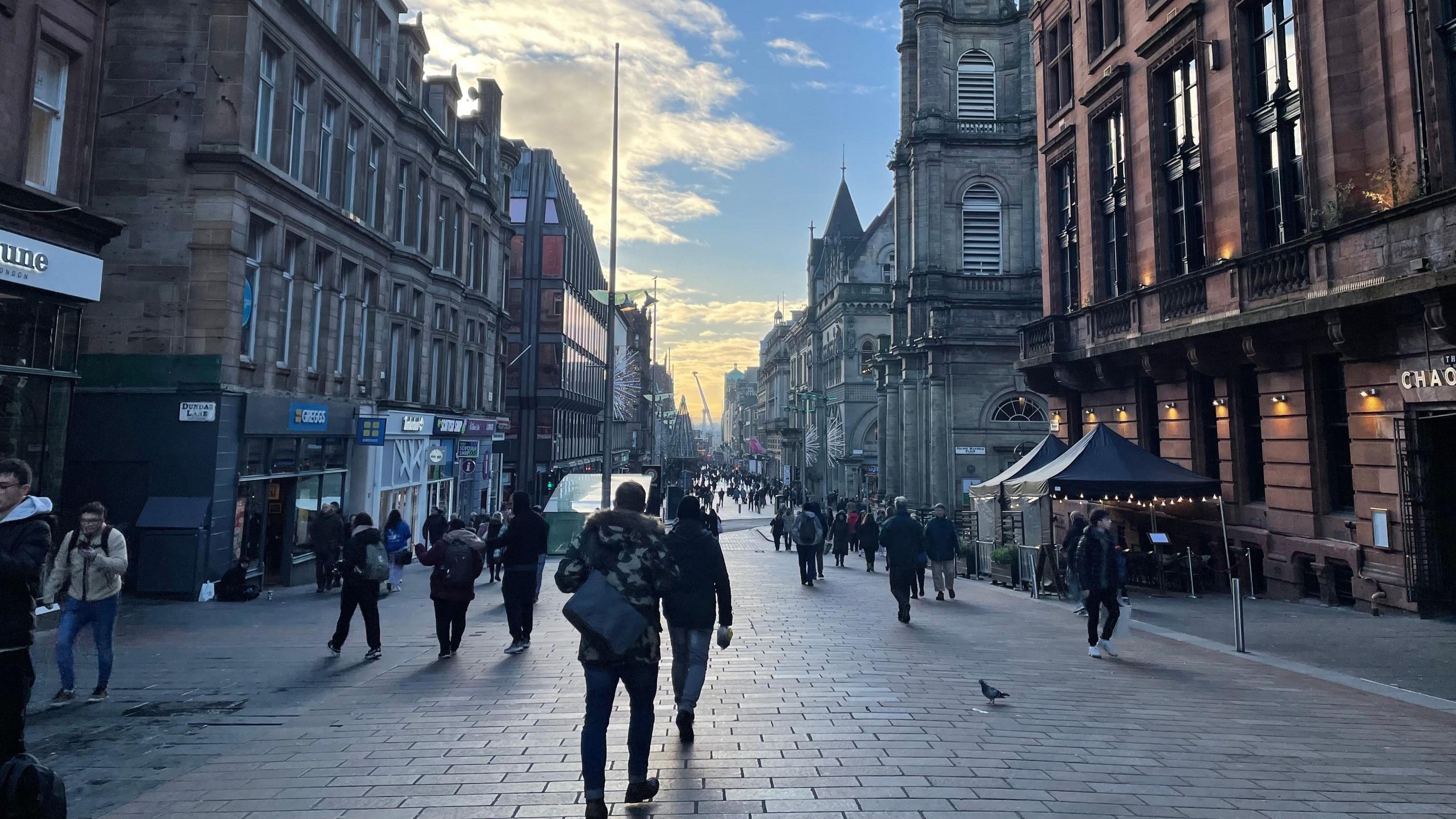 A view looking down a busy street, with people milling about and going into various shops