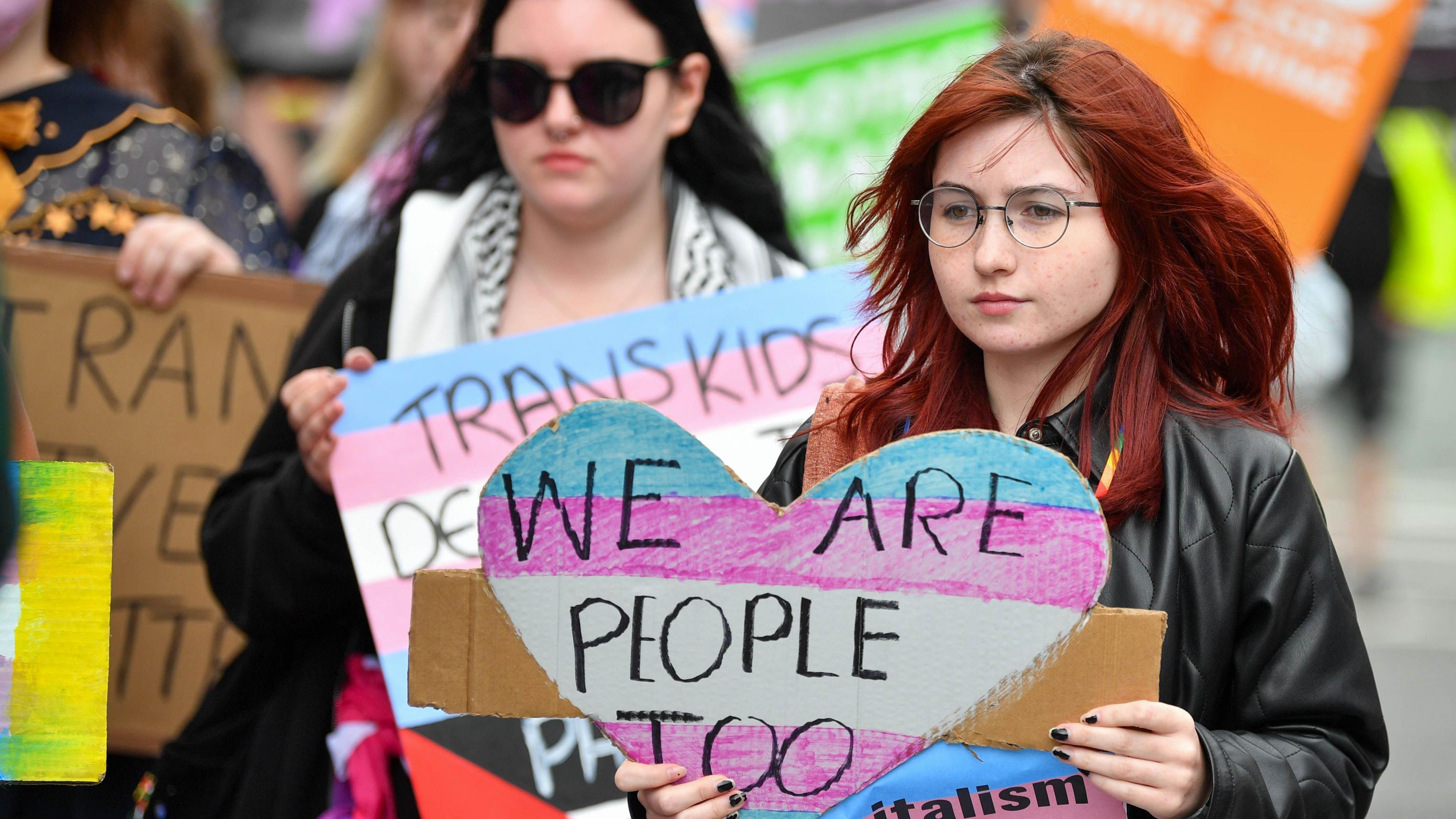 People are holding banners. One says we are people too. 