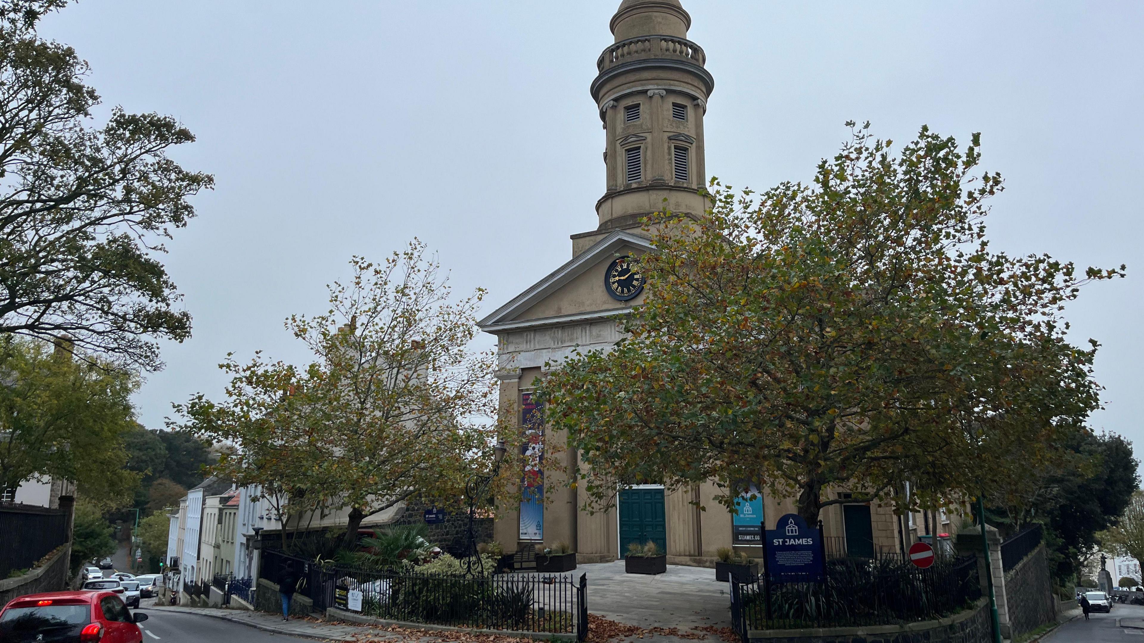 A brown building with a clockface and two trees in the foreground. 