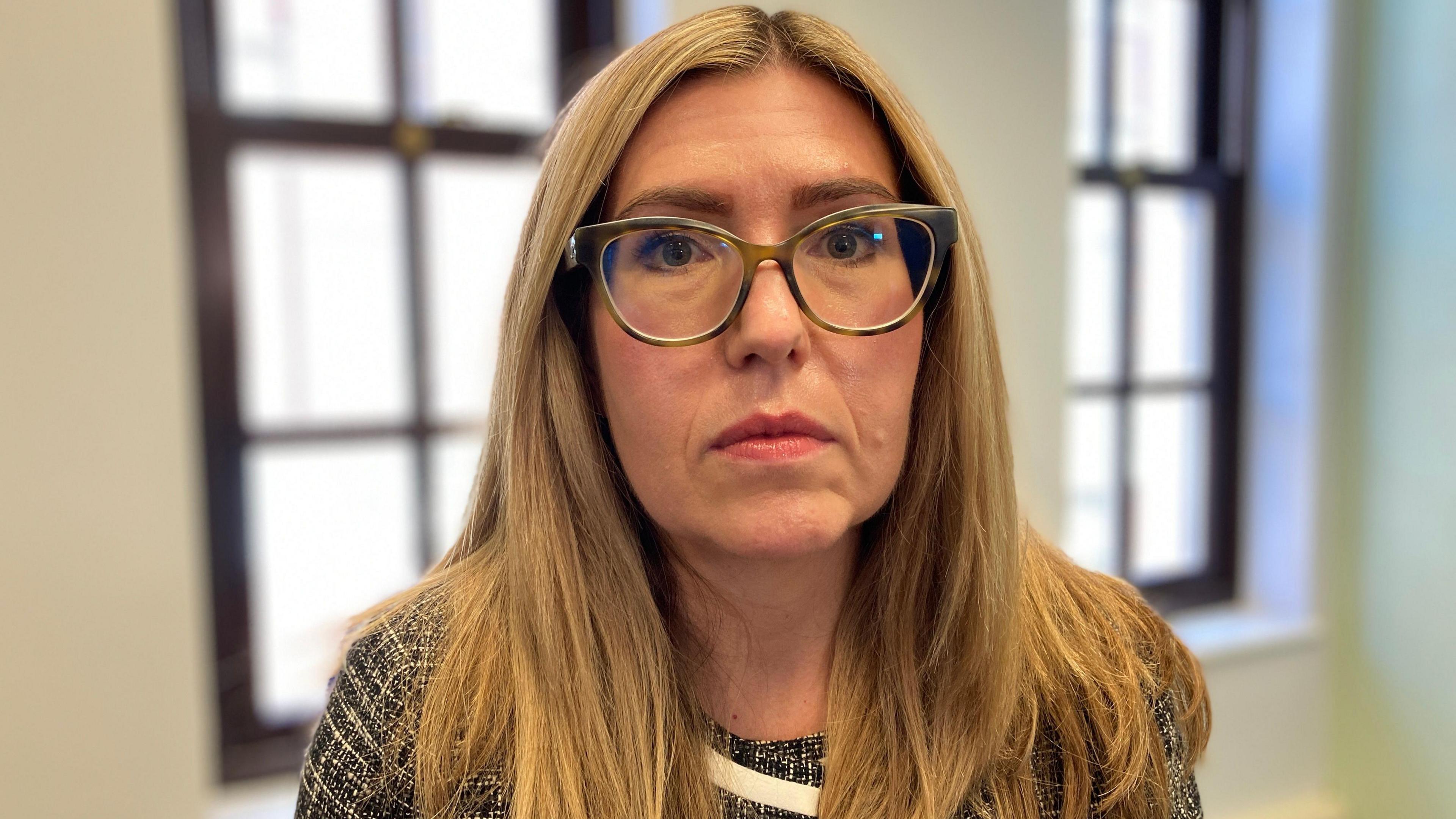 Charlotte Caulton-Scott wearing a black and white knitted jacket. She has long blonde hair and is wearing glasses.