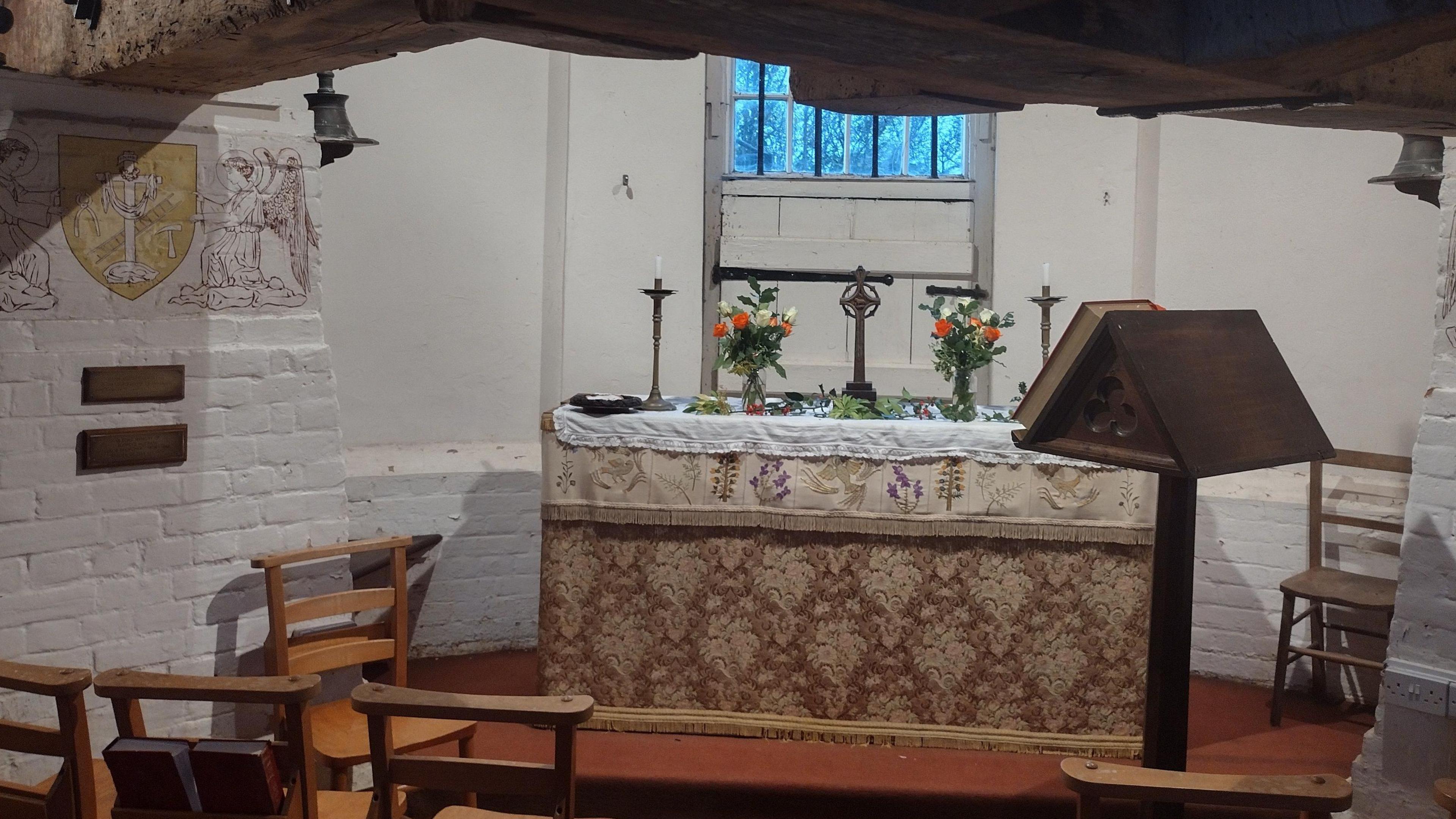 An image of the consecrated church inside the roundhouse of the Reigate Heath Windmill. An altar can be seen with candles and flowers, while rows of chairs are also visible.