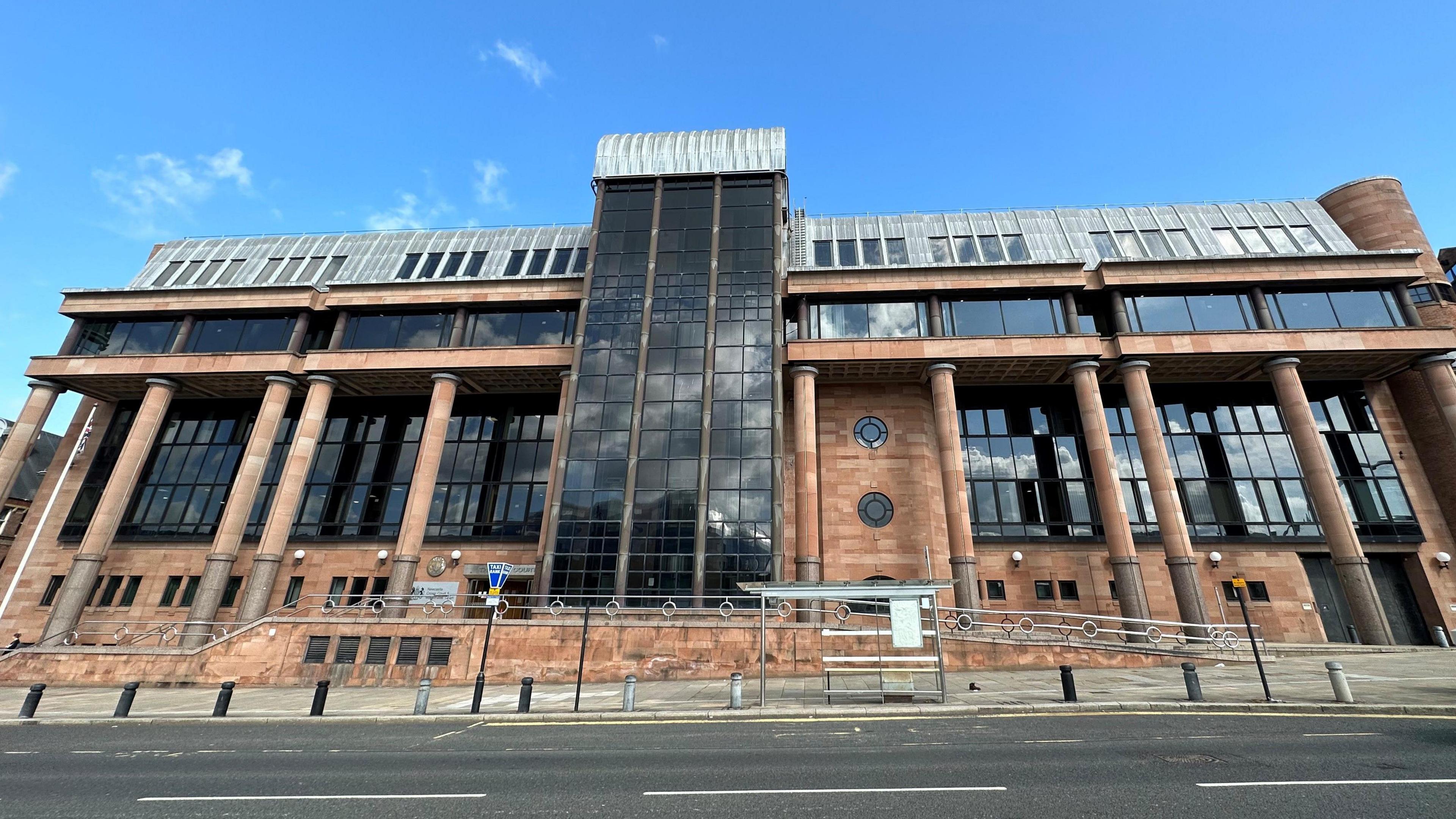 An imposing court building made from light red stone with large dark windows and a silver roof