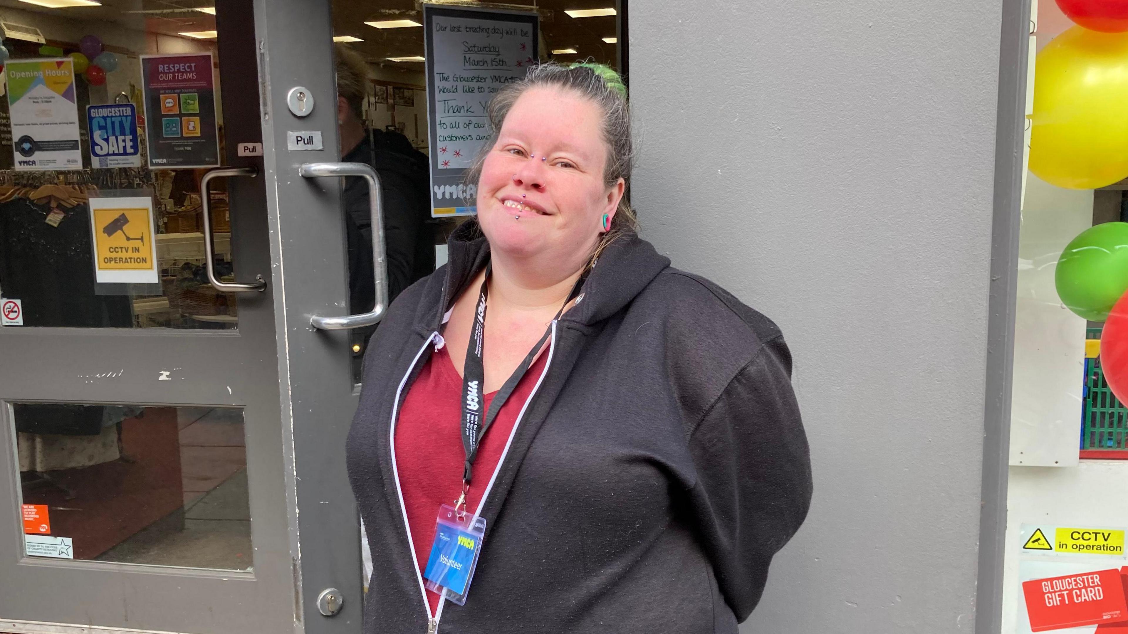 A photo showing volunteer worker Carley Load stood outside a YMCA charity shop in Gloucester