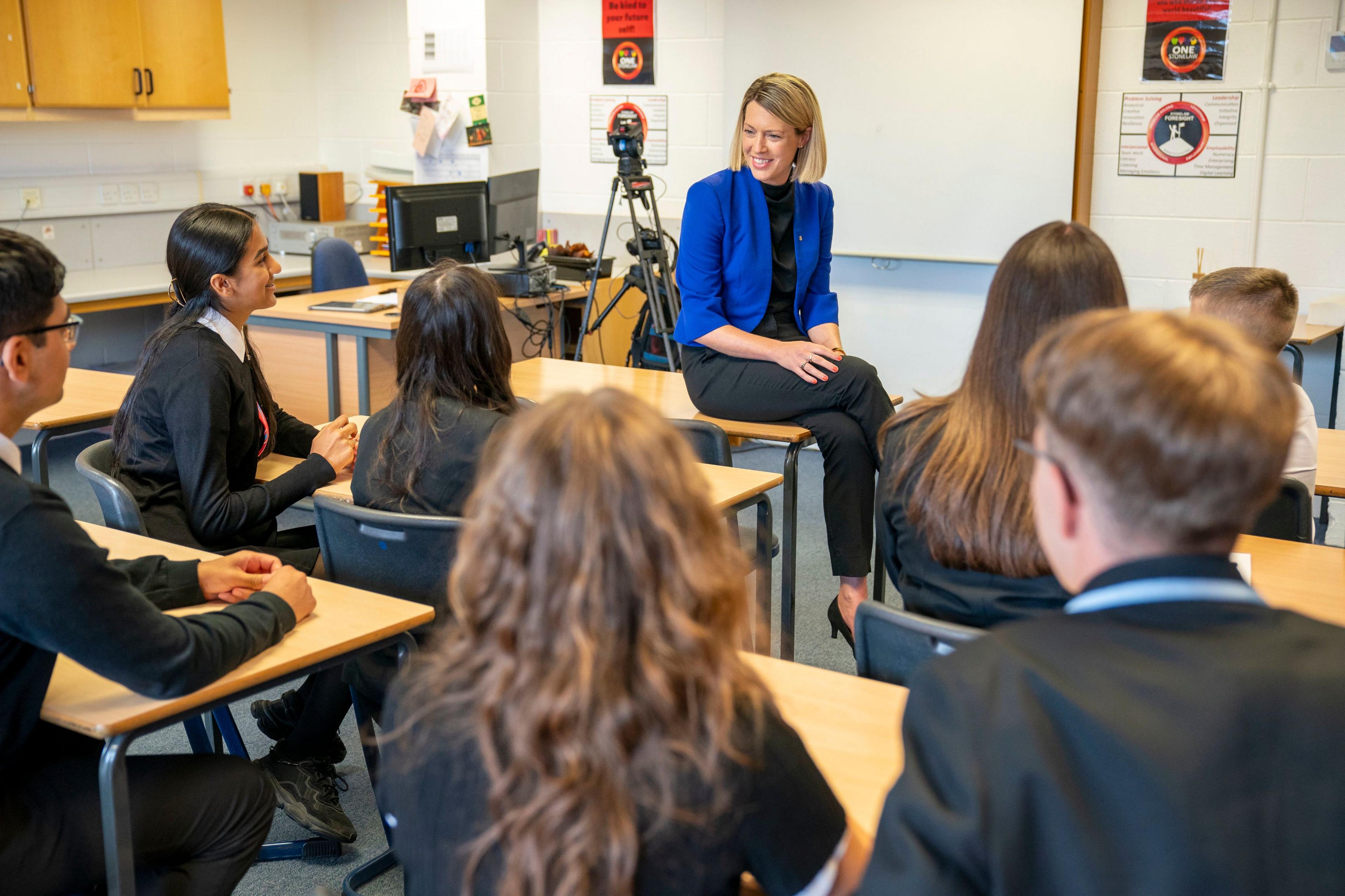 Education Secretary Jenny Gilruth sitting on a school desk in a classroom with pupils