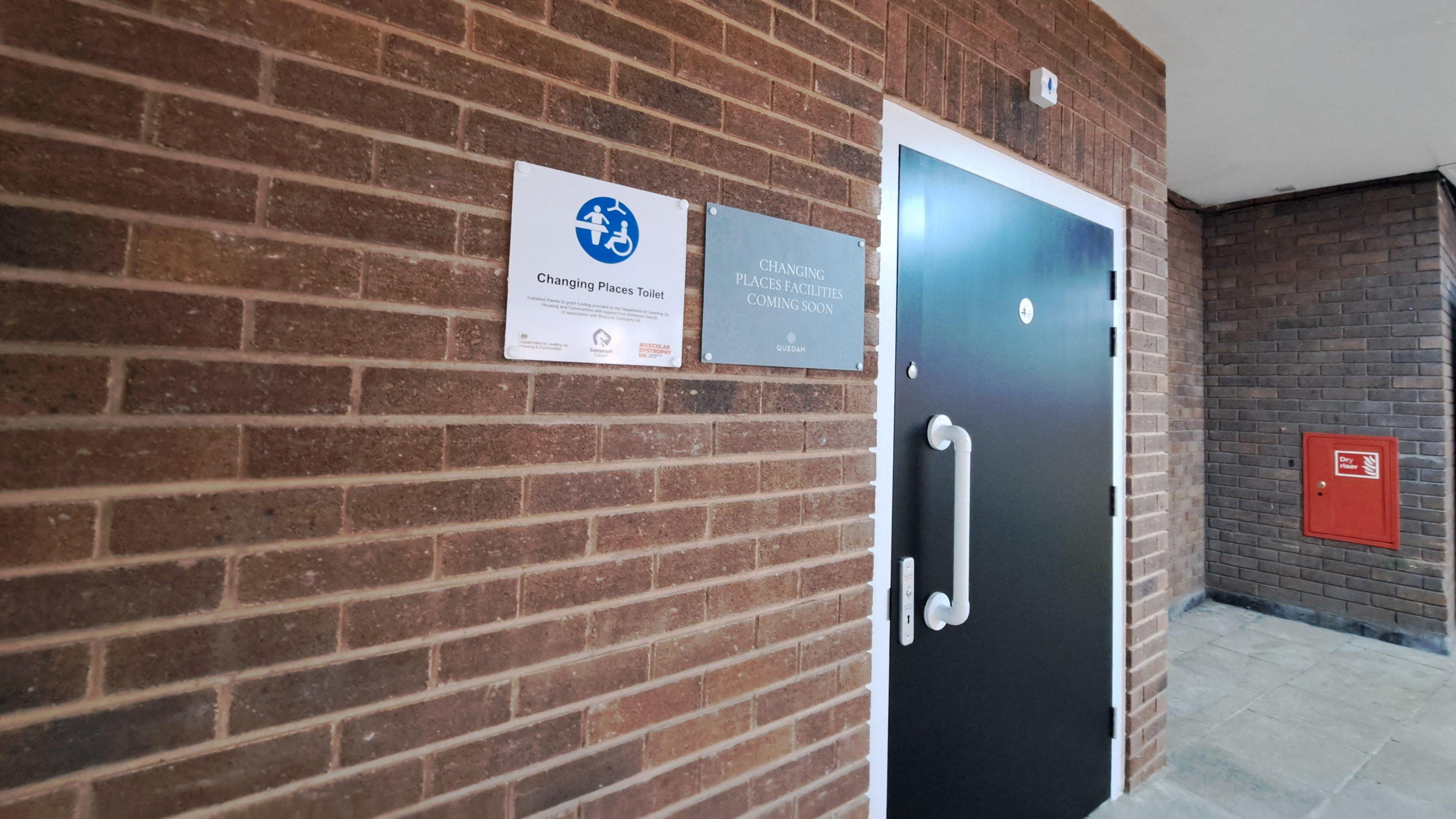 A red brick wall with a black door and a changing places toilet sign