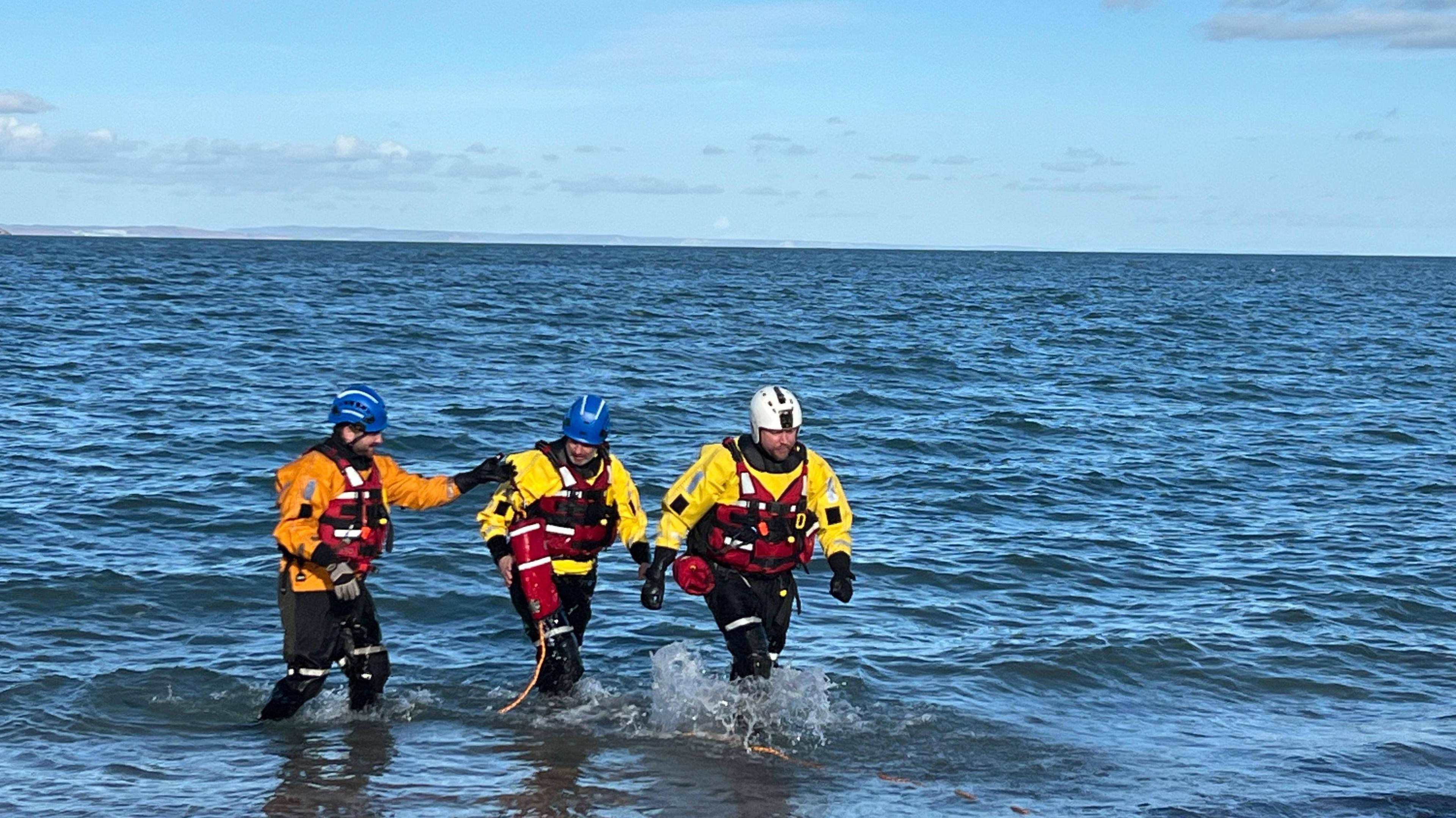 Three coastguards walking out of the water. 