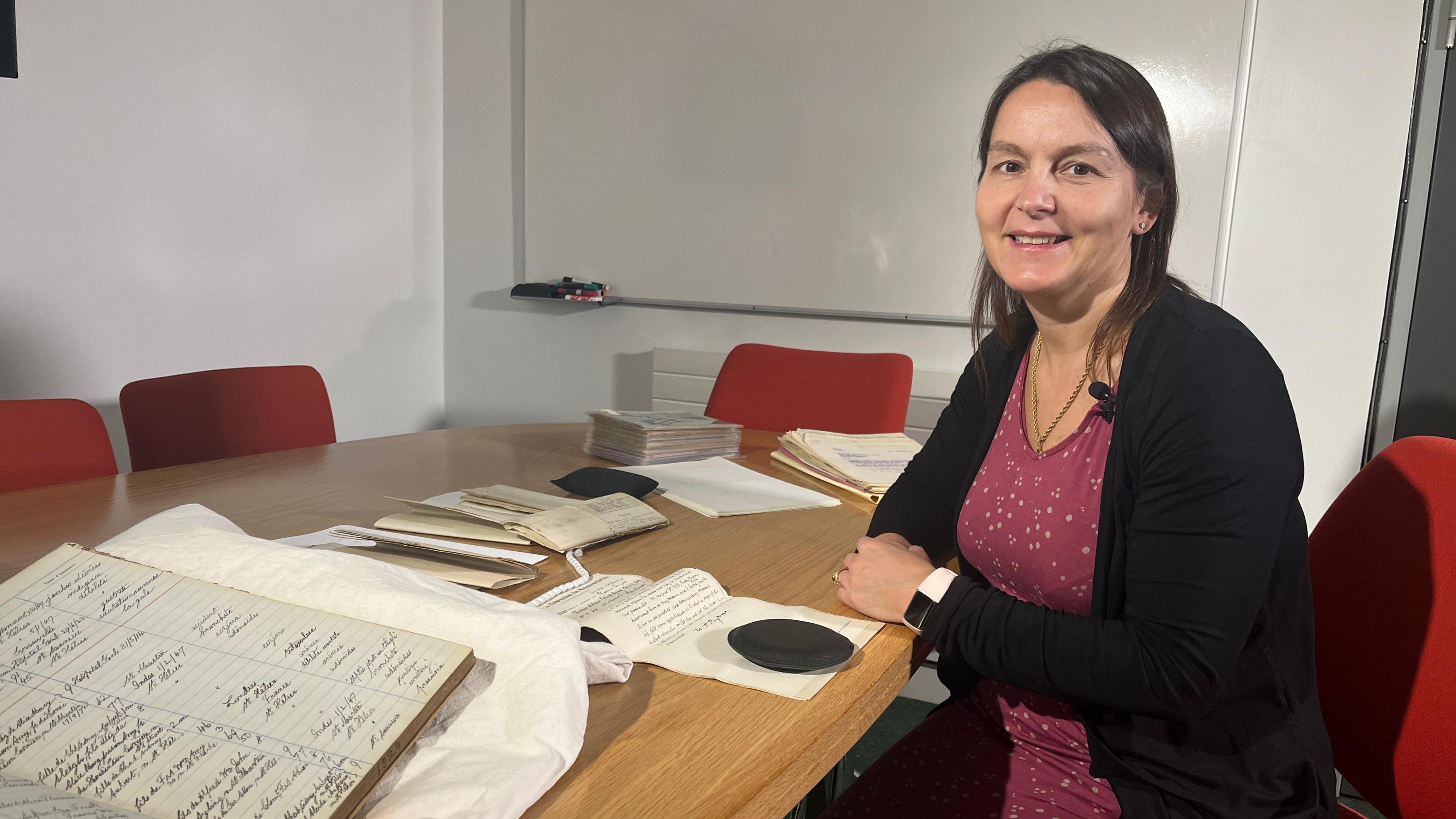 Linda Romeril - a woman sat at a desk with old records in front of her.