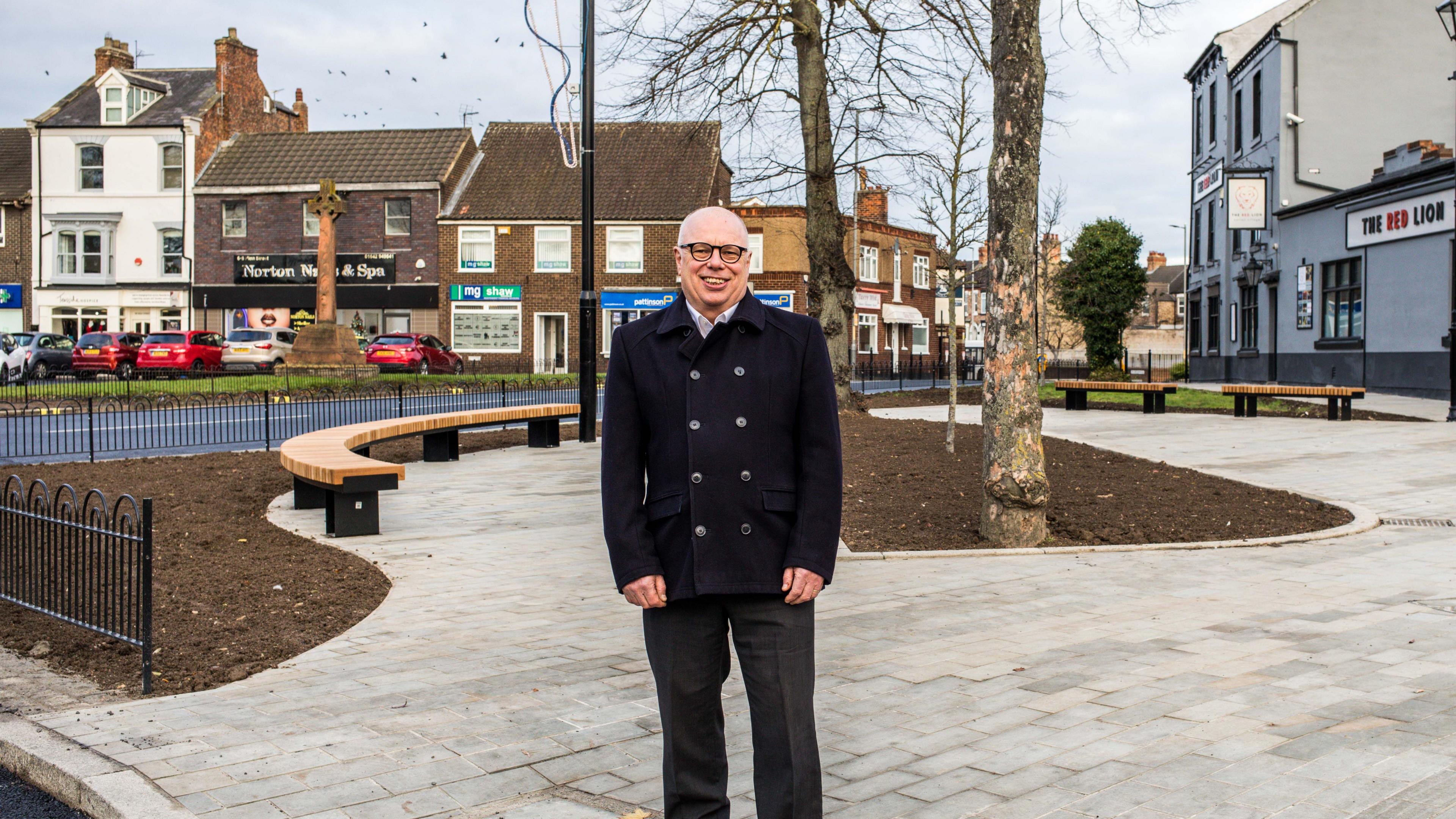 Nigel Cooke standing in the new public space at Harland Space. He is wearing a double-fronted jacket and glasses. He is smiling at the camera.