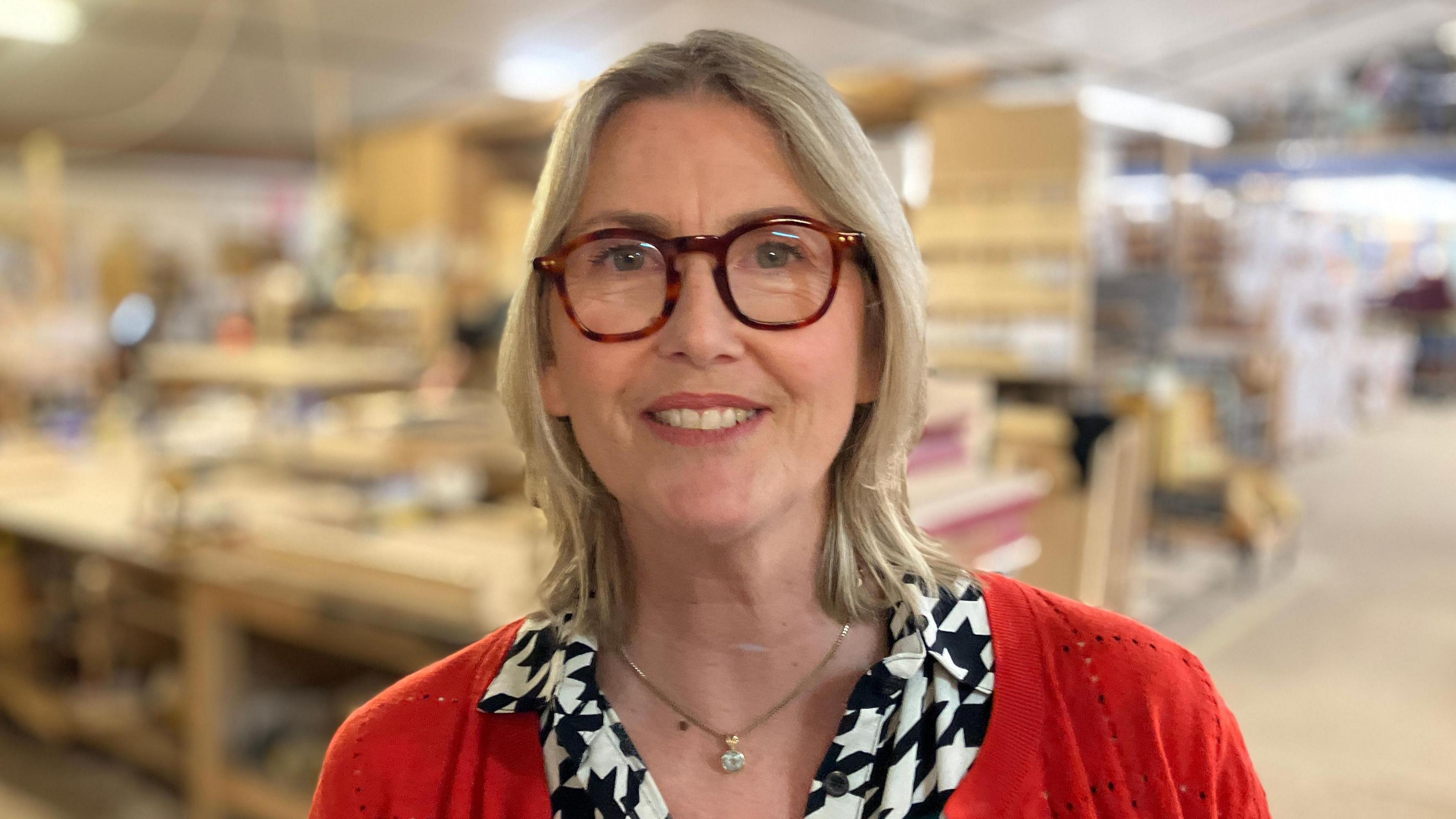 Rachael Waring wearing glasses and a red top standing in her furniture workshop.