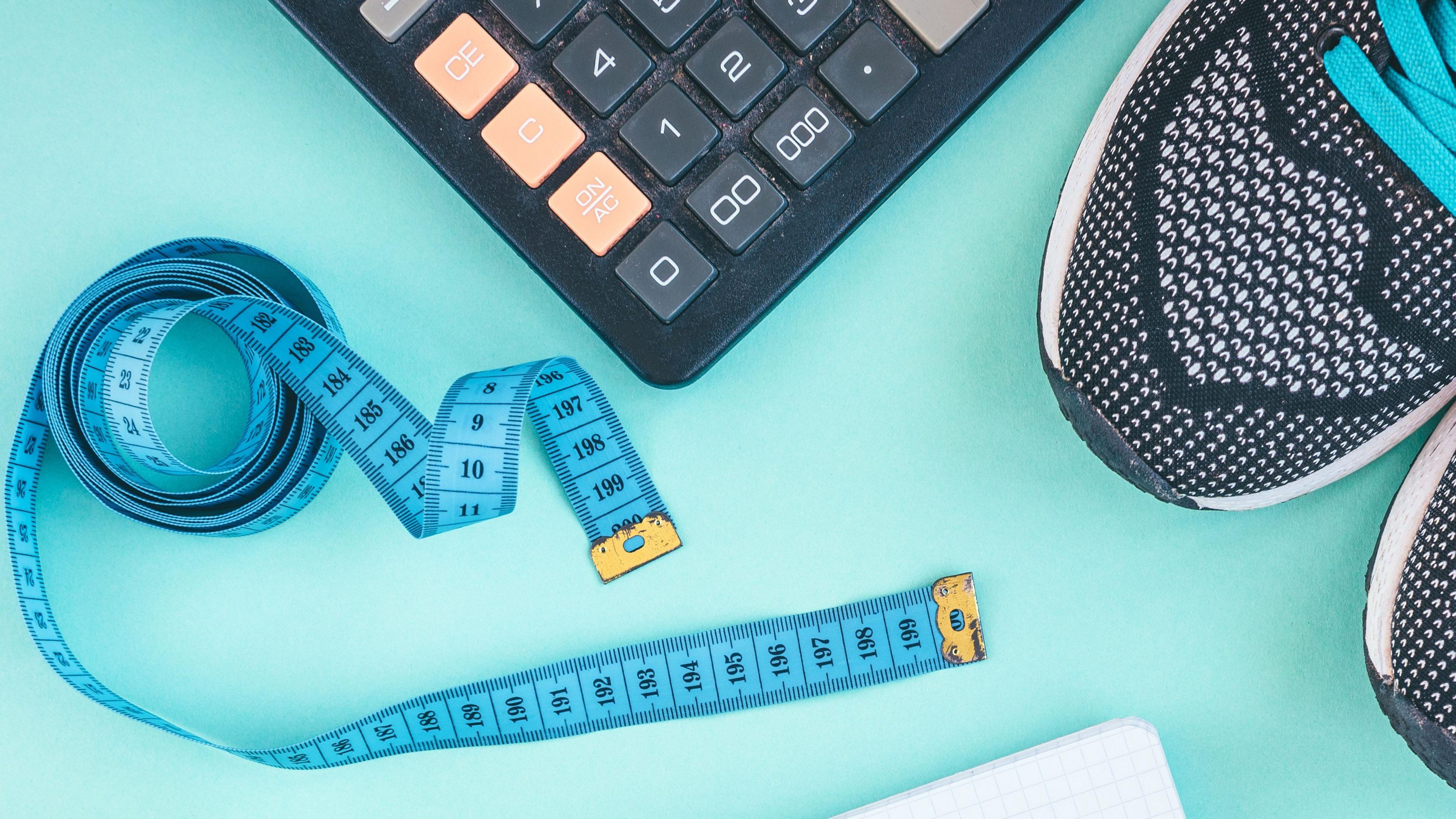 Tape measure, trainers and calculator on a light blue background