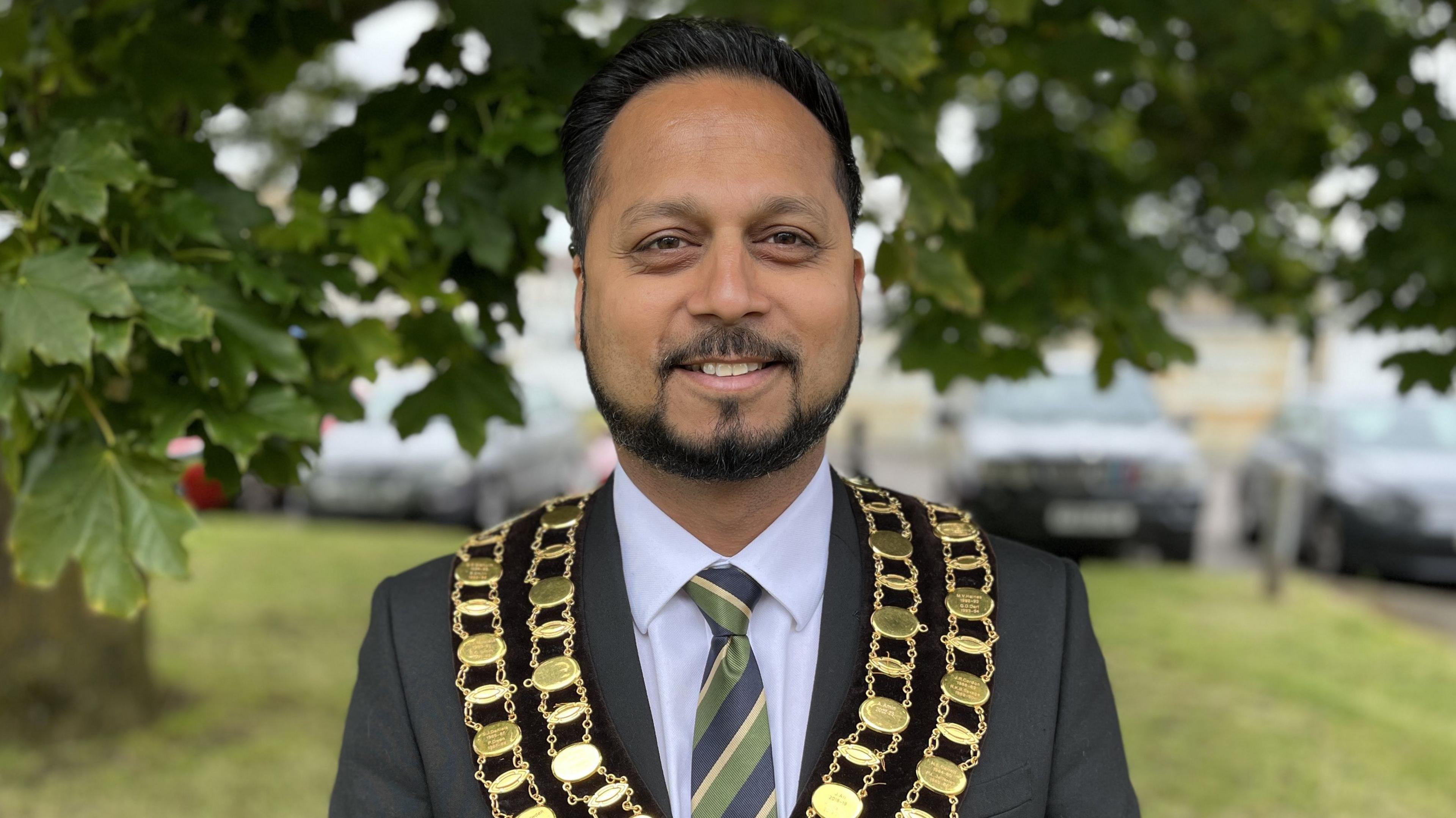 Mayor of Swindon, Cllr Imtiyaz Shaikh, wearing his gold chains over a grey suit with a blue, green and gold tie