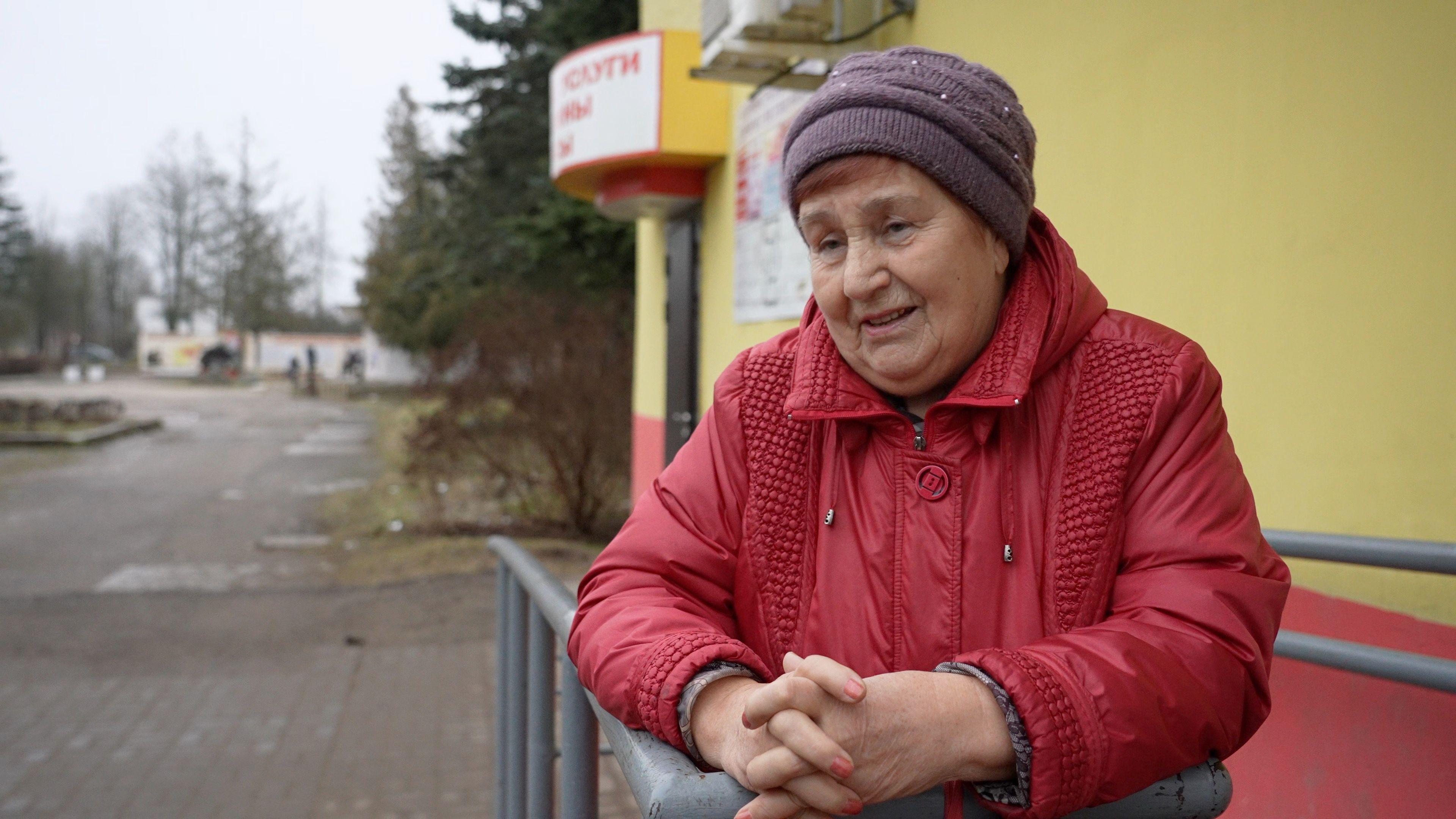 An elderly Belarusian lady wearing a red coat and a purple hat. 