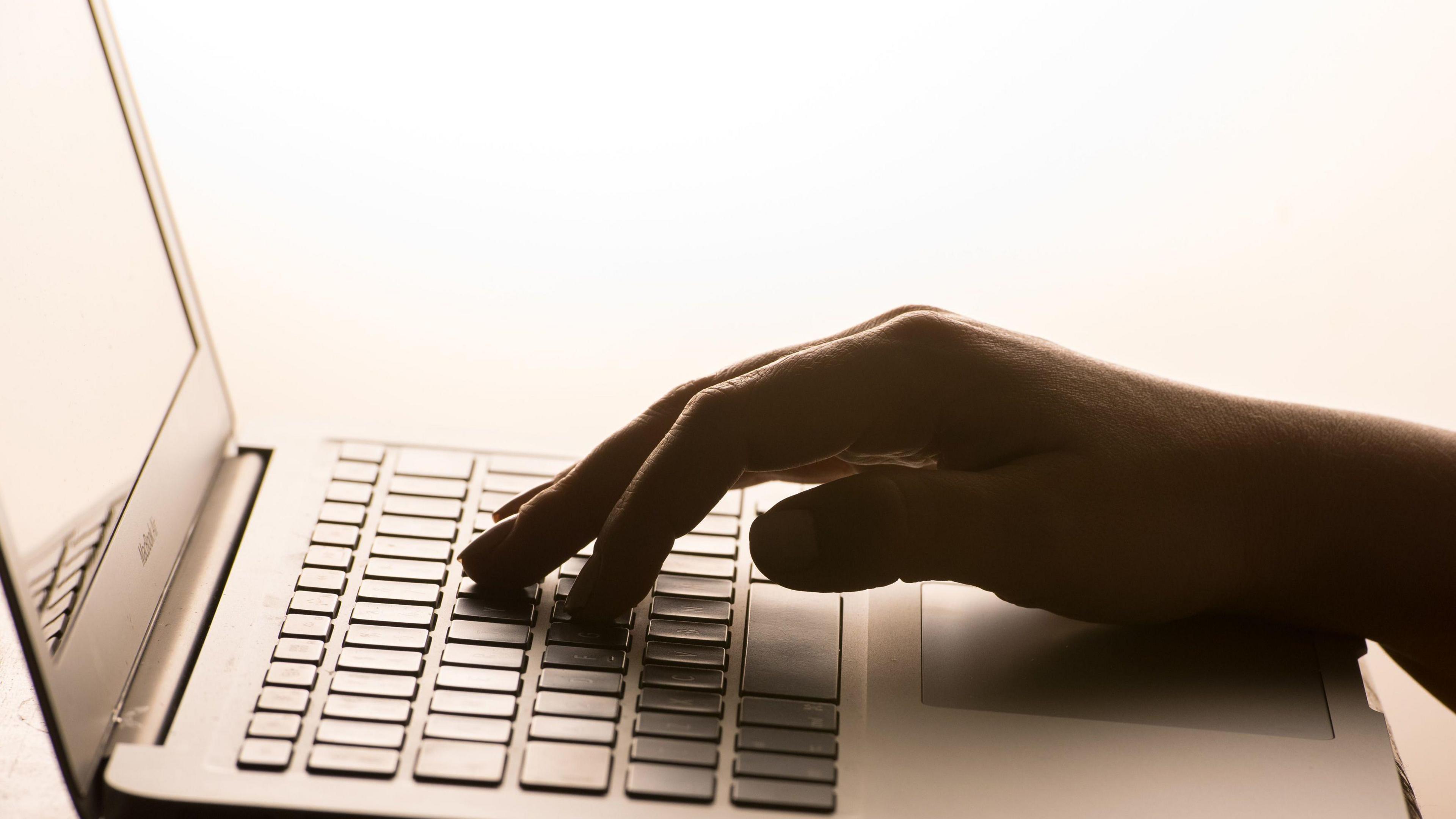 A picture of a hand typing on a keyboard. It is a silver laptop.