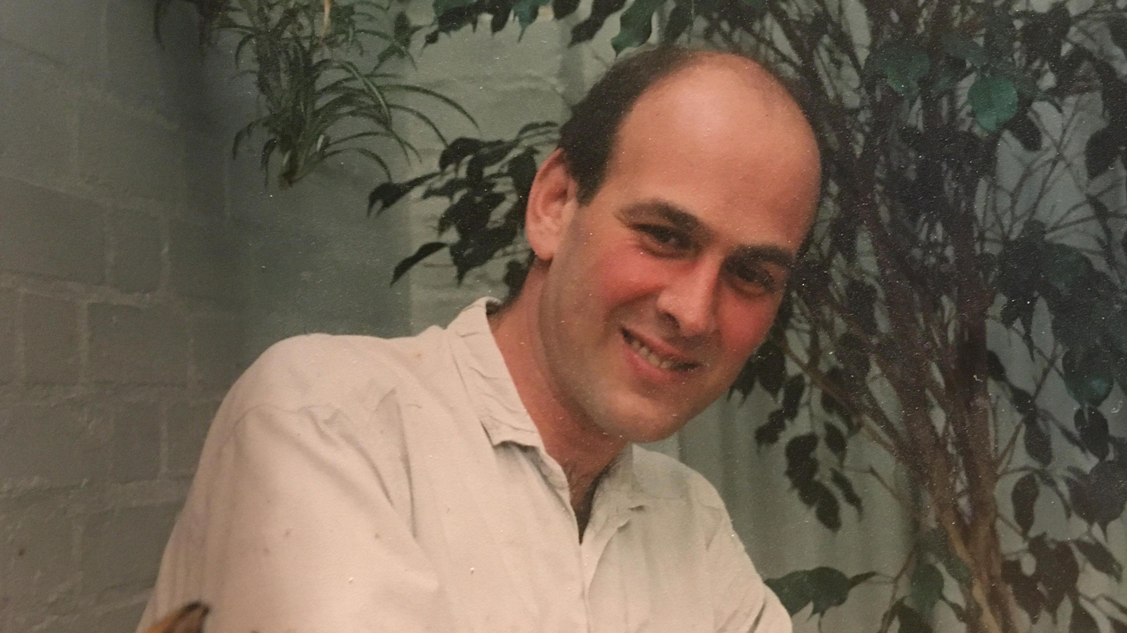 An old photo of Michael, who is wearing a white shirt and smiling at the camera.