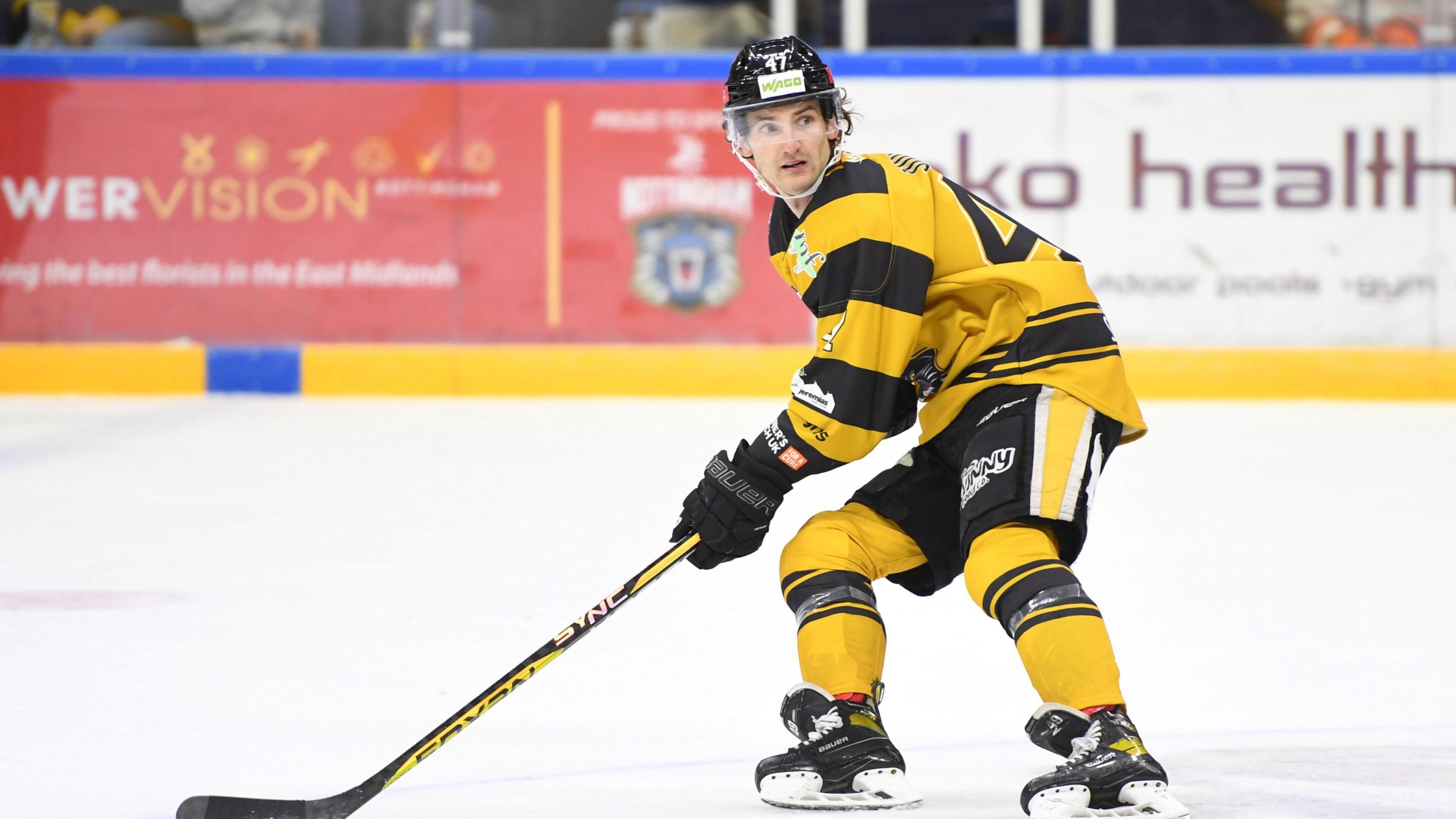 Ice hockey player Adam Johnson on the ice during a match. He is dressed in a yellow jersey with black shorts, yellow socks and black skates. His ice hockey stick is also black and yellow