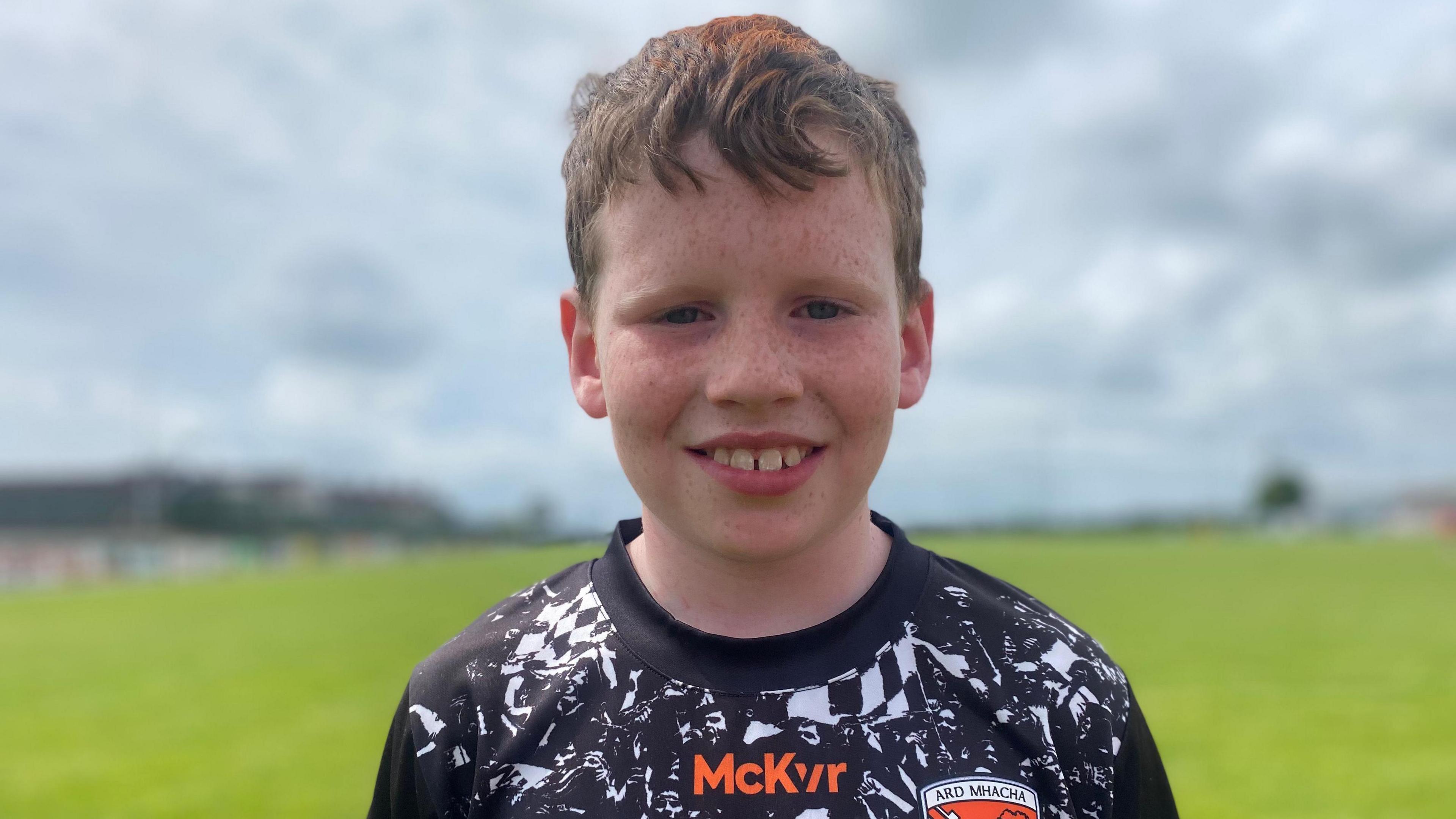 Liam is smiling directly into the camera. He is wearing a black and white GAA jersey with orange writing. 