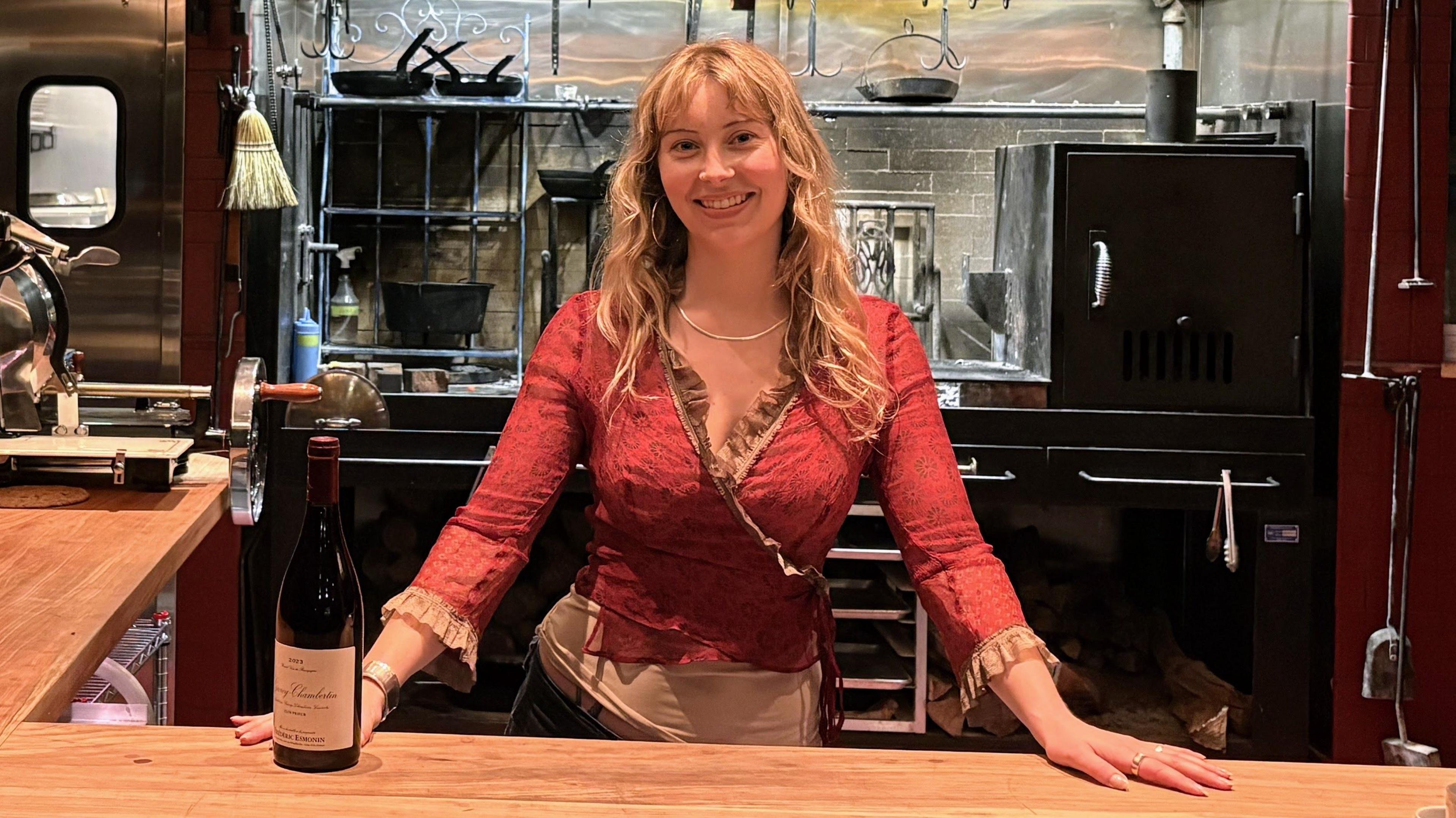 Caroline Kraetzer stands behind a bar, with her hands on the counter.