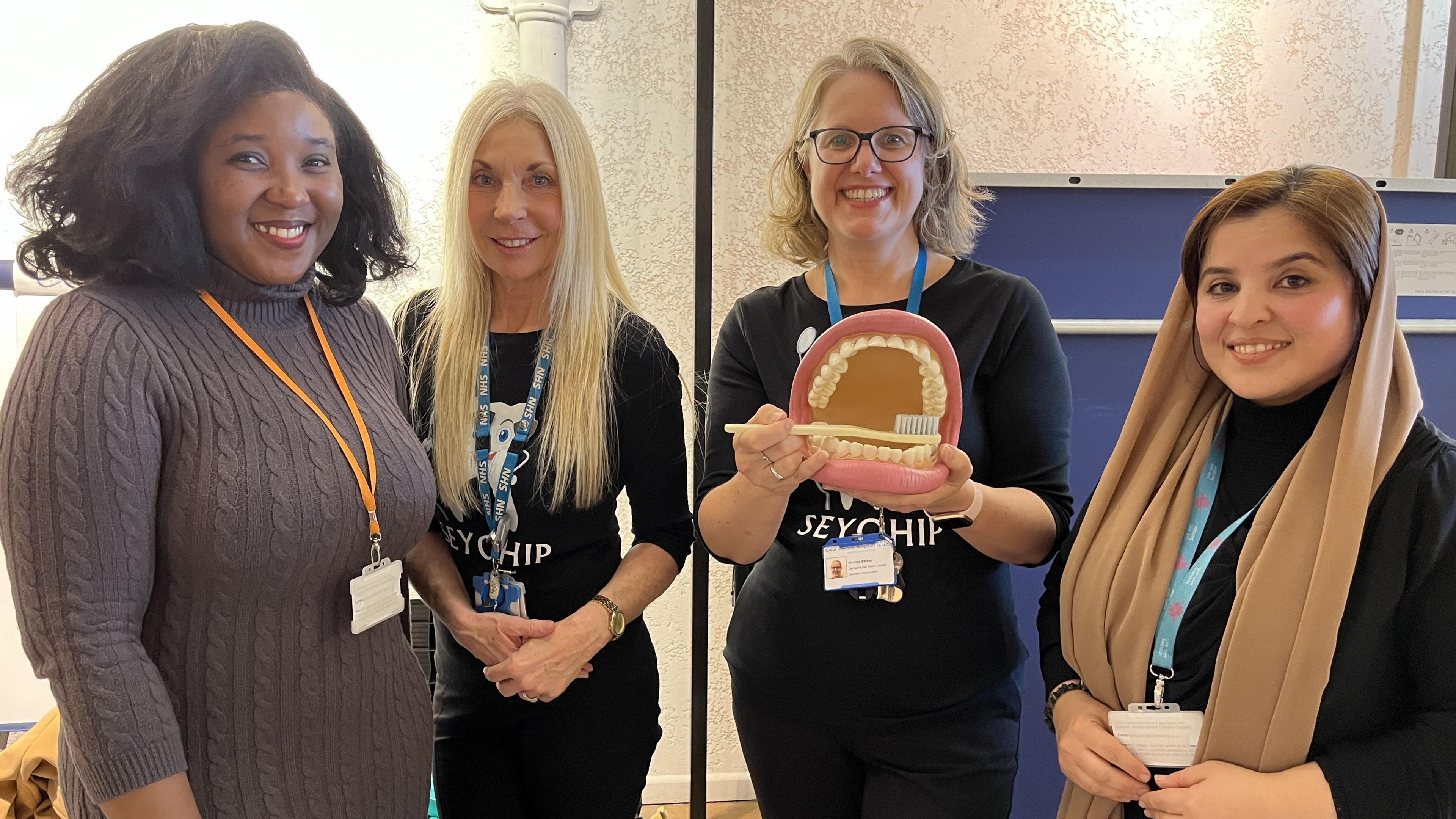 Four dental health specialists from Swindon Borough Council and Great Western Hospital NHS Foundation Trust smiling and holding a large model mouth with a toothbrush