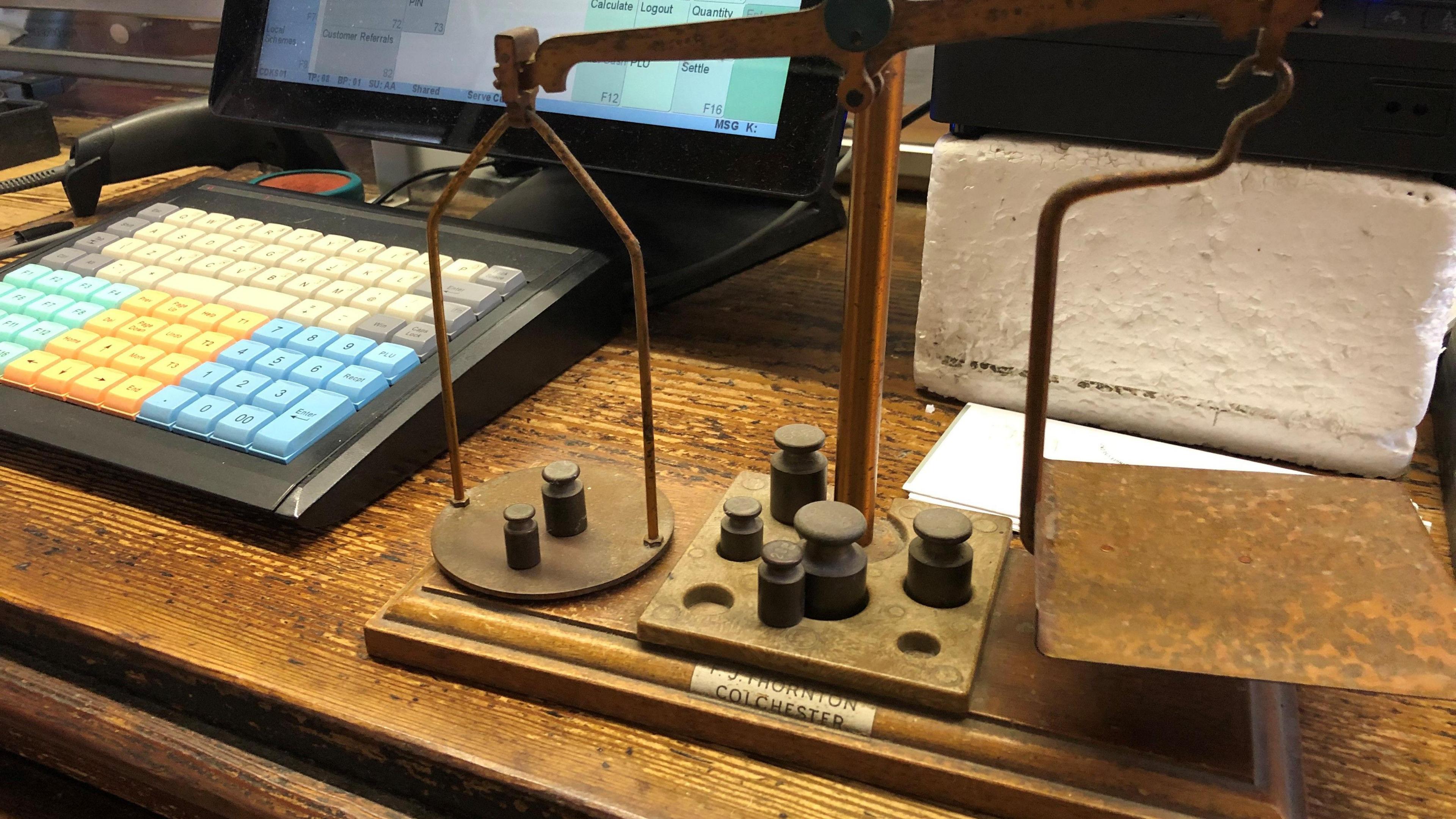 Old set of metal scales next to a post office computer on a wooden desk.