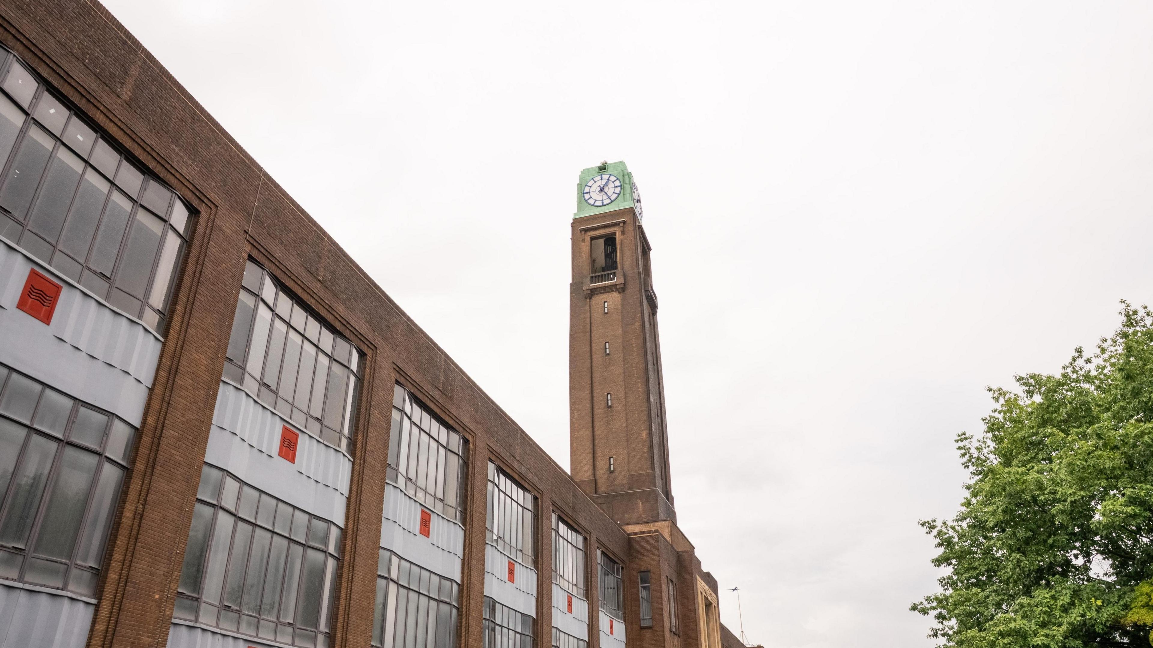 A photo looking up at of an Art Deco clock with brown brick and a green metal structure with a white face and blue hands.