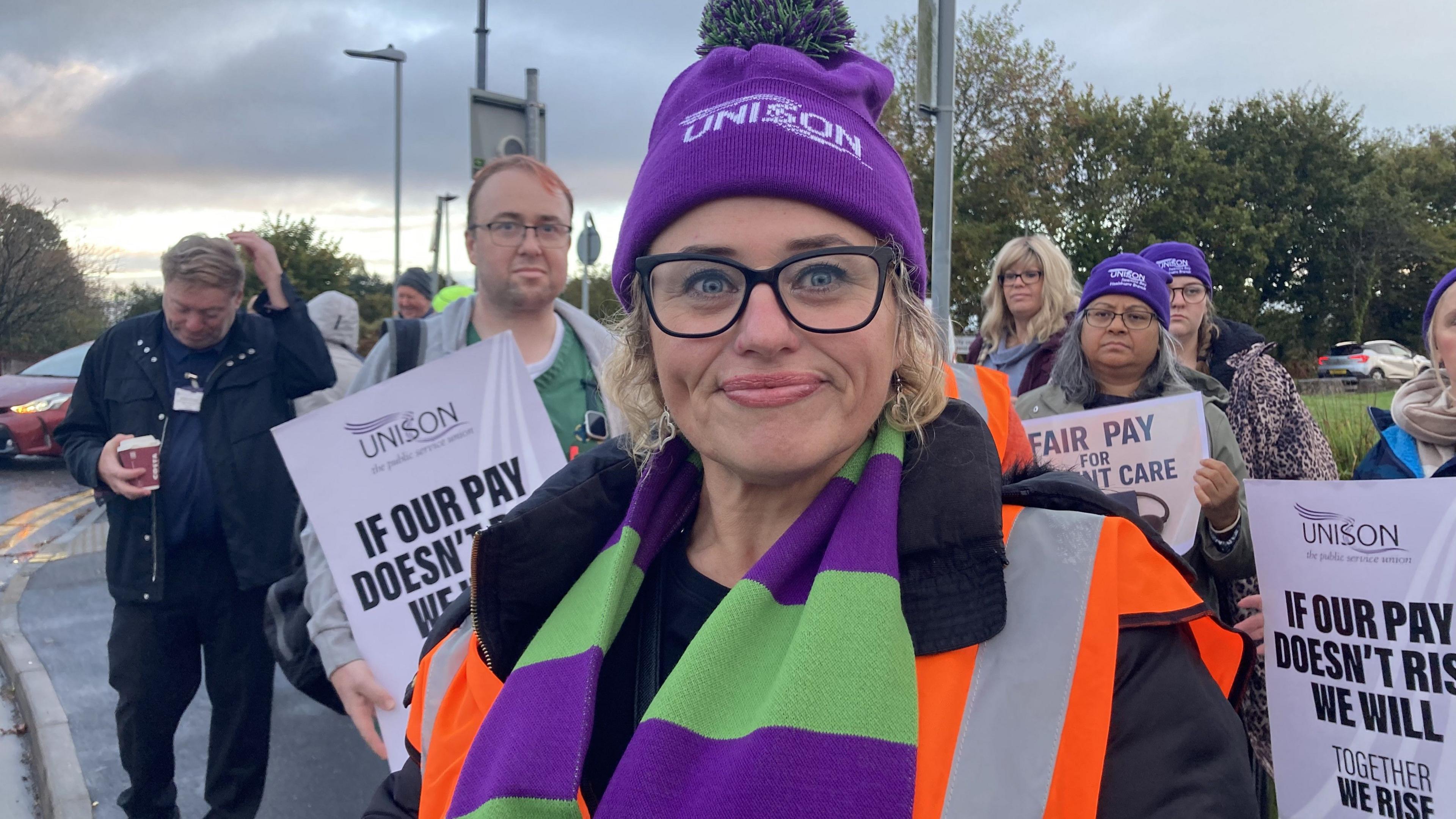 Mae Lianne Owen yn gwisgo het borffor gyda'r enw UNISON arno. Mae ganddi sbectol sgwar du a sgarff porffor a gwyrdd. Mae'n sefyll o flaen sawl person arall sydd hefyd yn protestio.