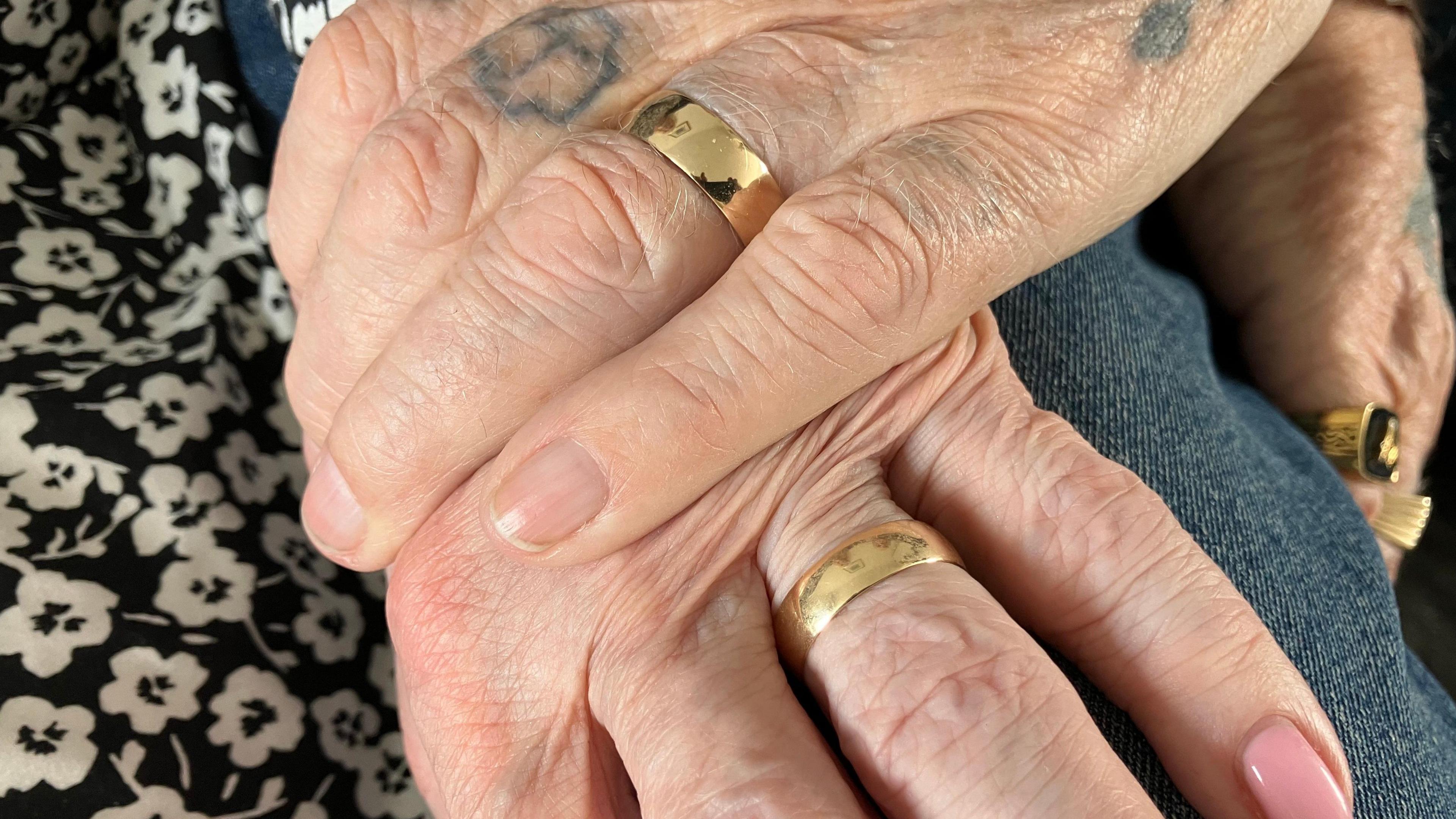A close up of two hands, both have wedding rings on
