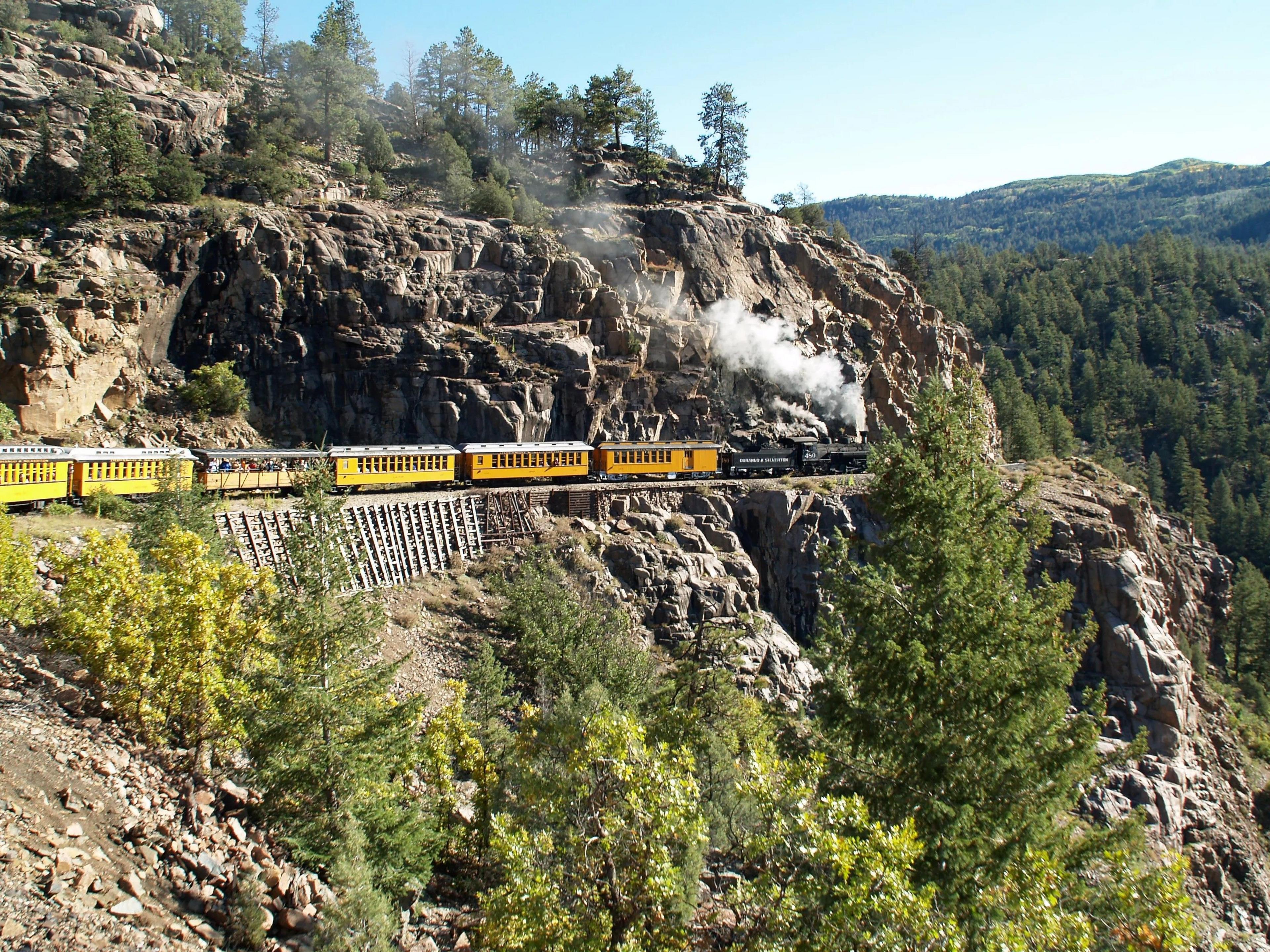 A steam train picks its way on tracks along the side of a mountain