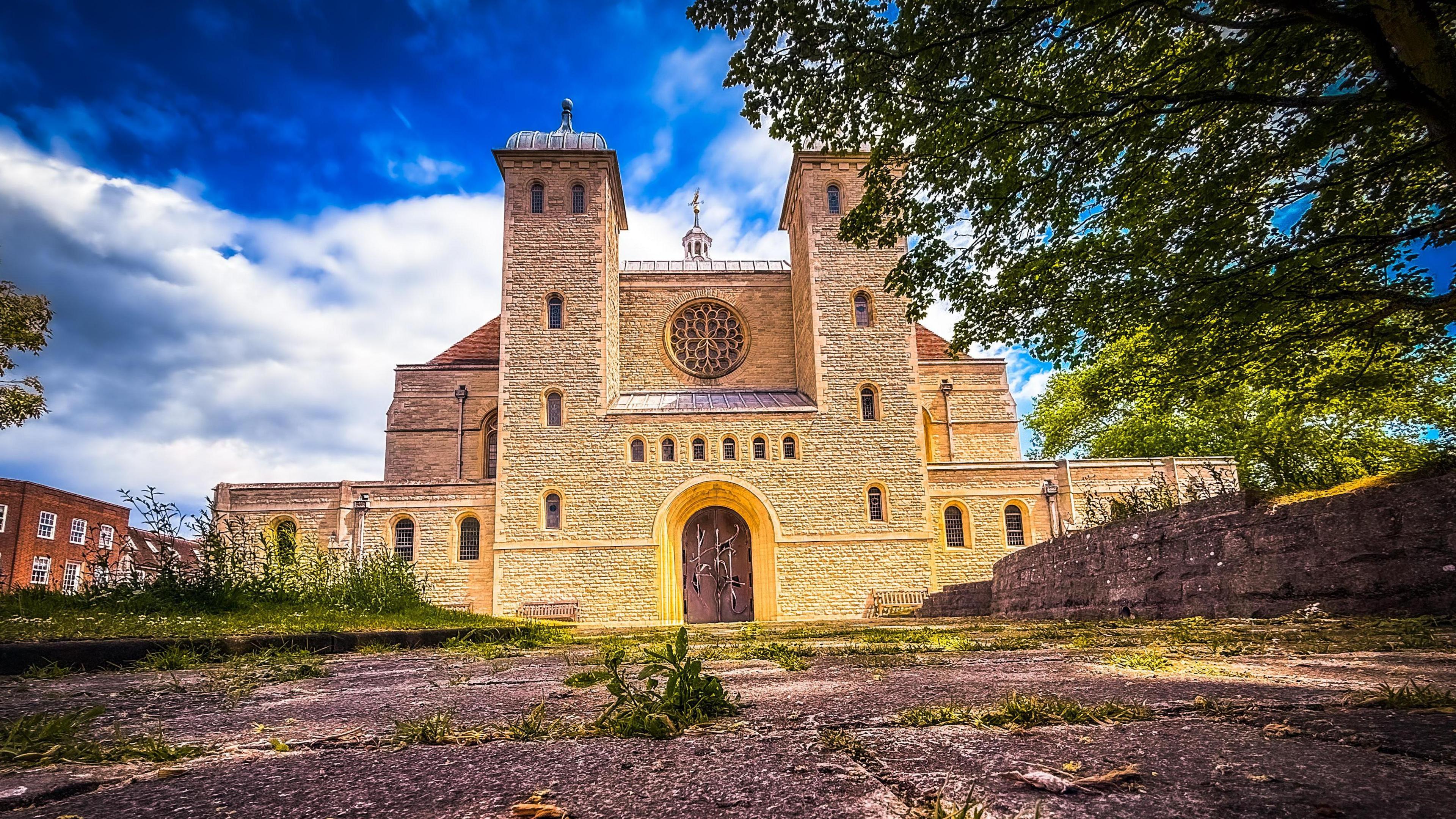 The front of a large cathedral with two towers either side of a circular stained-glass window, shot from a low angle and with a blue sky behind.