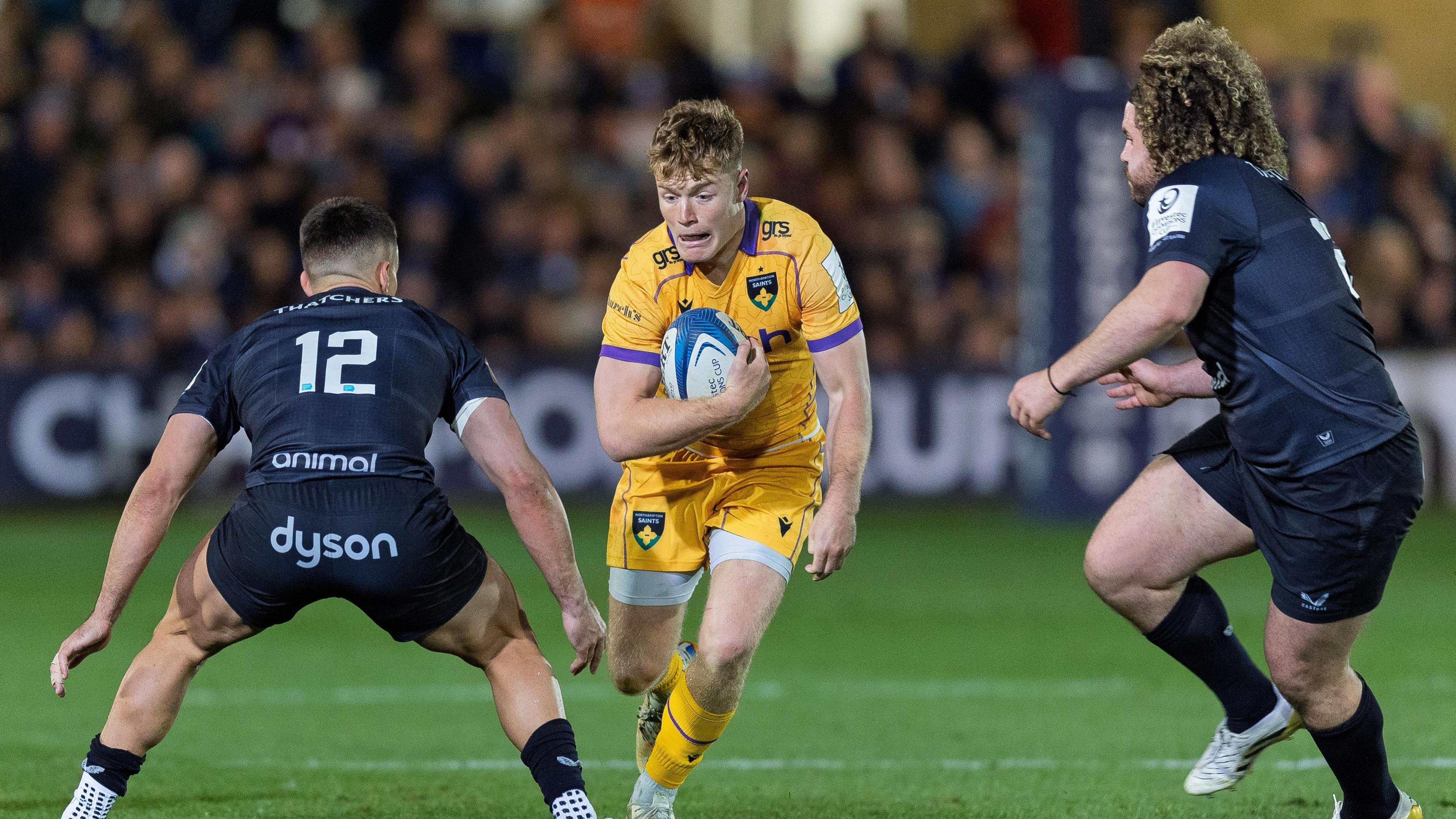 Fin Smith (centre) runs with the ball under his right arm close to his chest as a Bath player approaches from his left and right