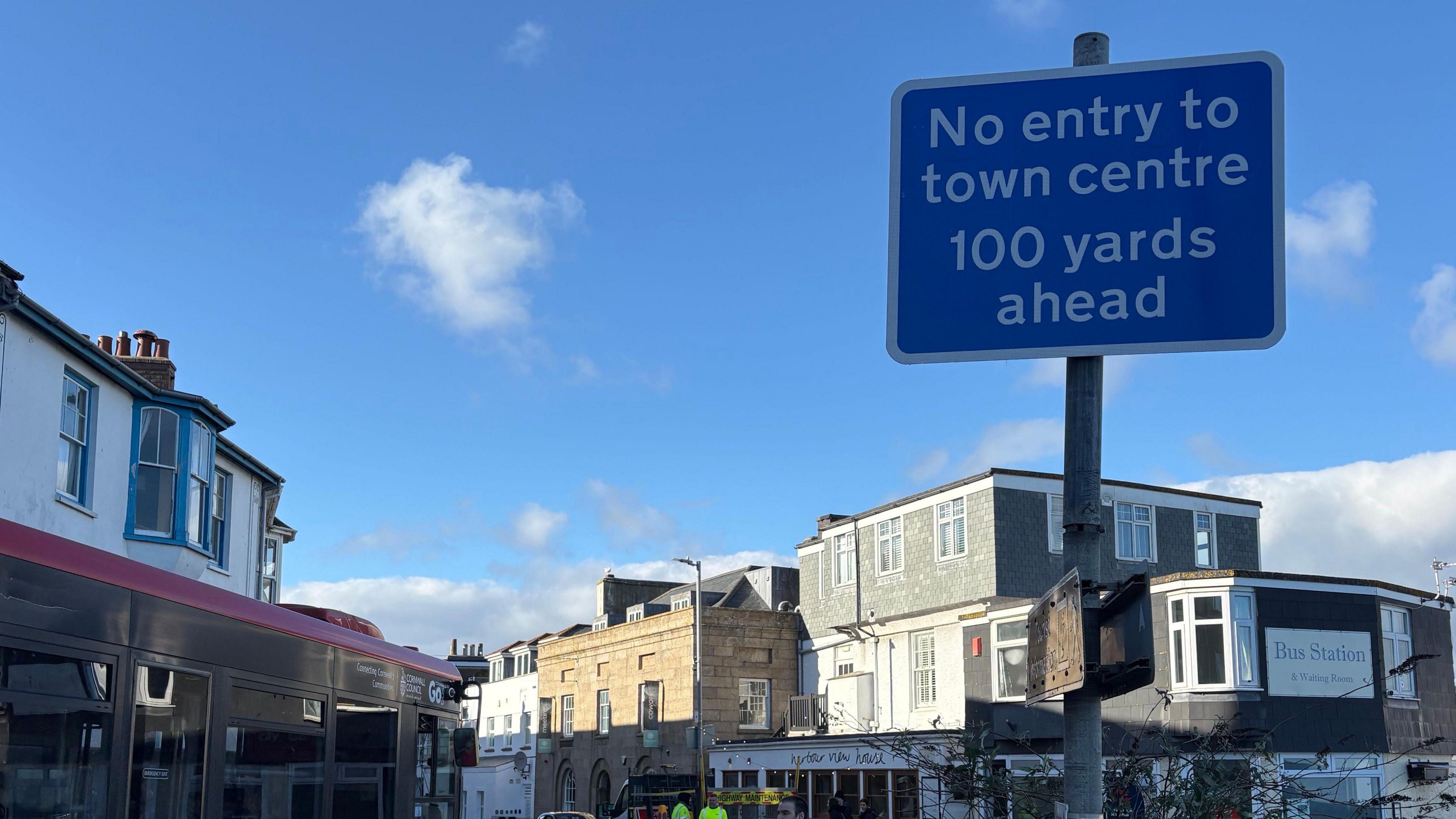 A blue road sign with white writing at the entrance to Tregenna Hill with shops in the distance. The sign reads: 'No entry to town centre 100 yards ahead'
