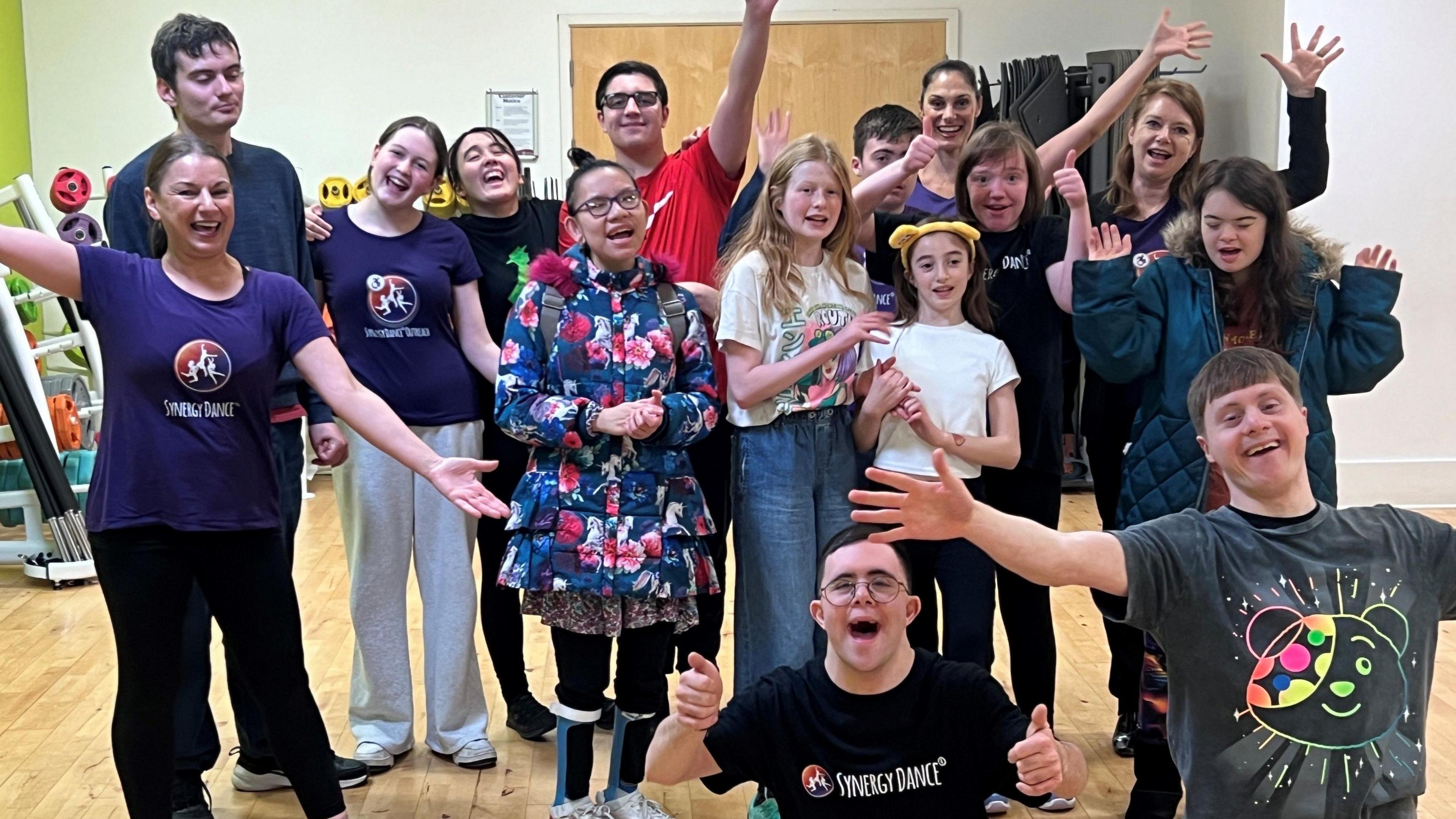 Group of children and teenagers smiling and waving their arms in celebration along with their dance teachers.