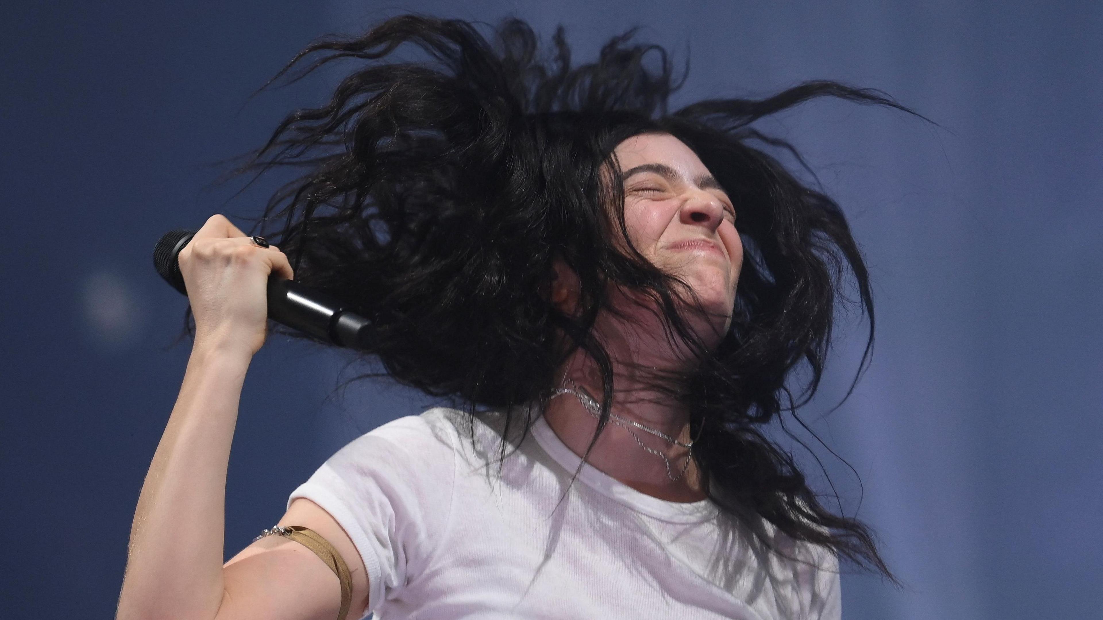 A close up of singer-songwriter Lorde. She has dark hair, is wearing a white T-shirt and is holding a microphone in one hand.