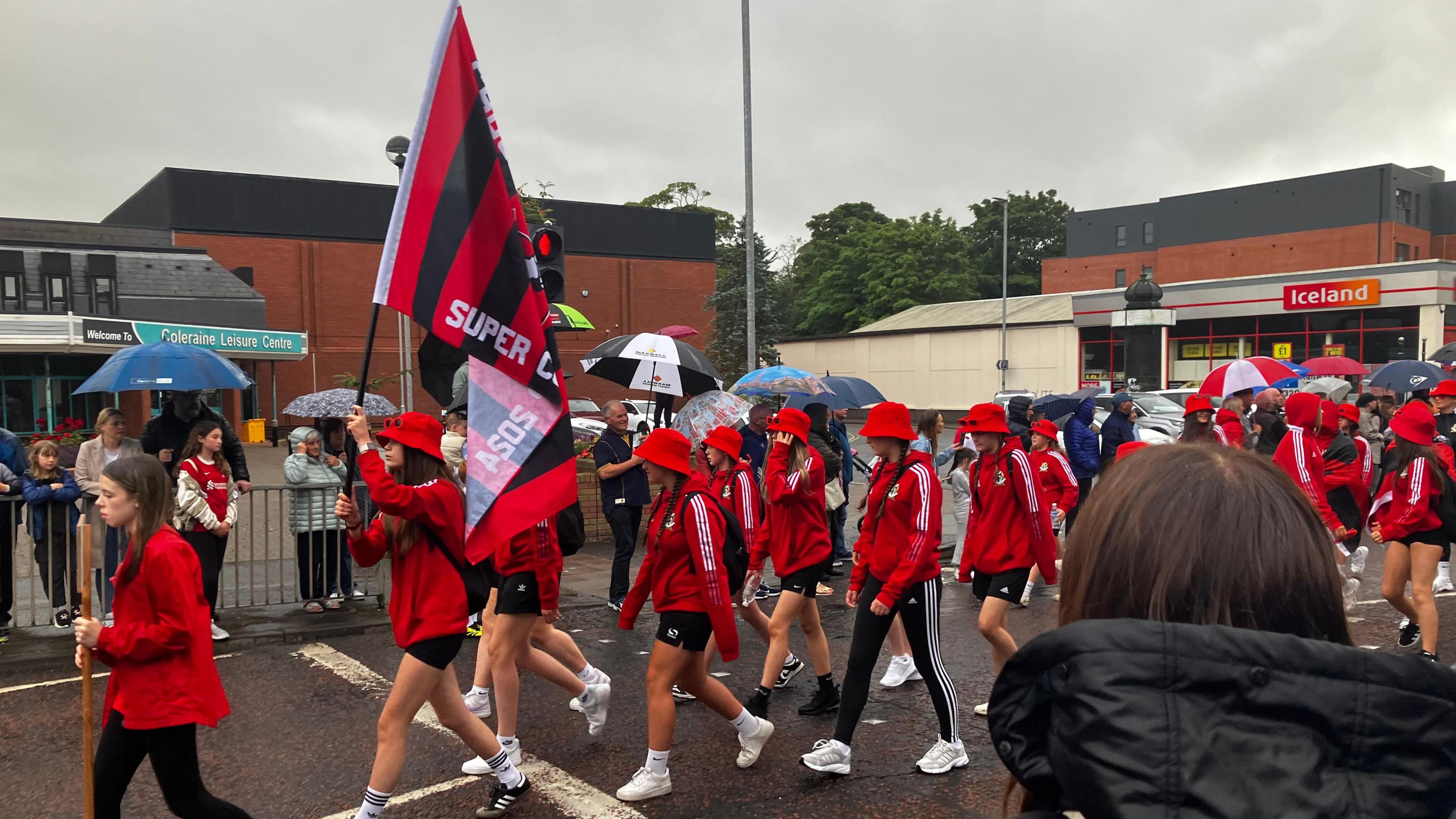 Flgas being carried by young girls from a football team, wearing red and black tracksuits