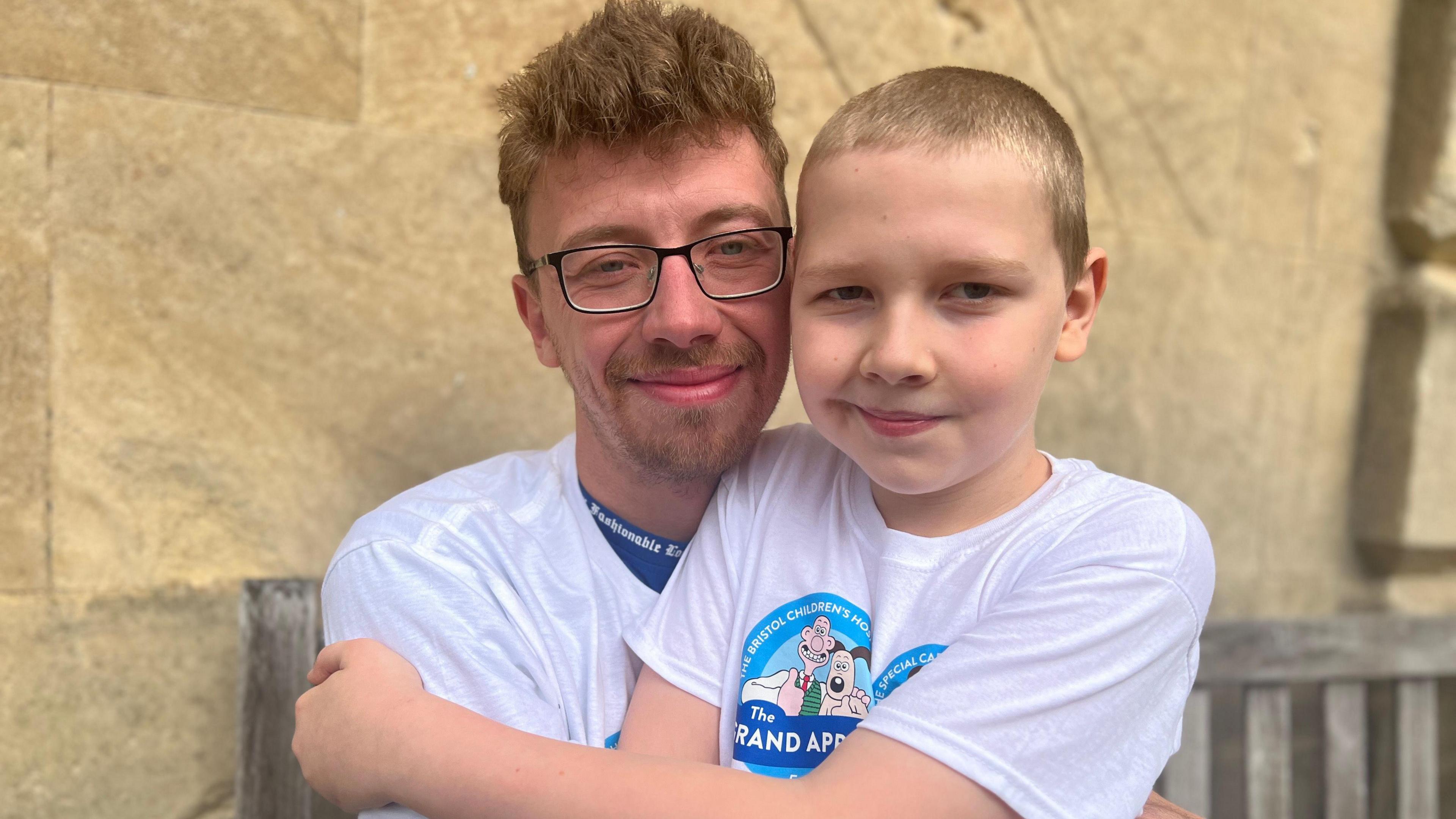 Harry Studley hugs his dad, Edward, as they sit on a bench against a brick wall