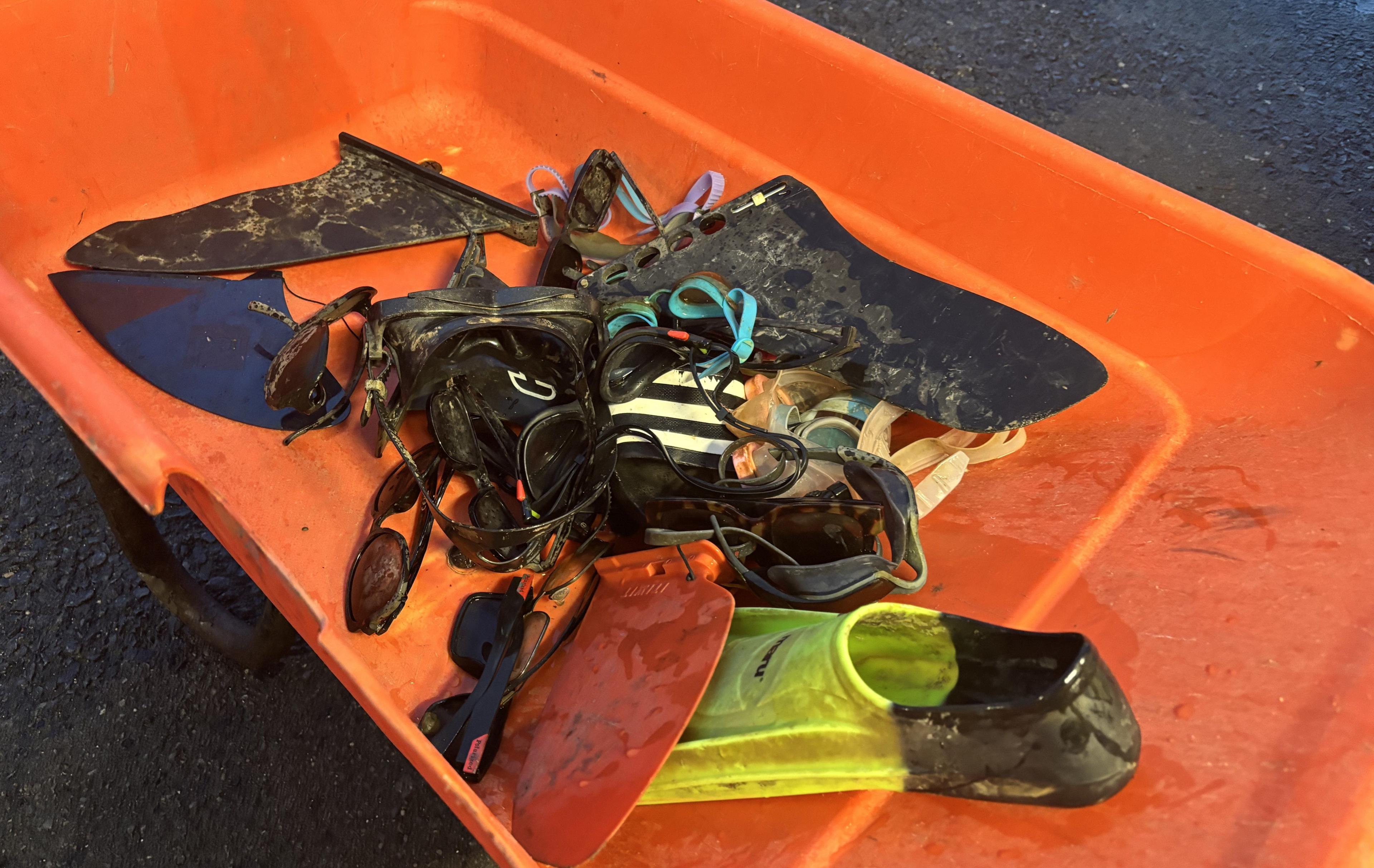 A orange wheelbarrow filled with a collection of goggles, flippers and sunglasses which were found at the bottom of the drained lake.