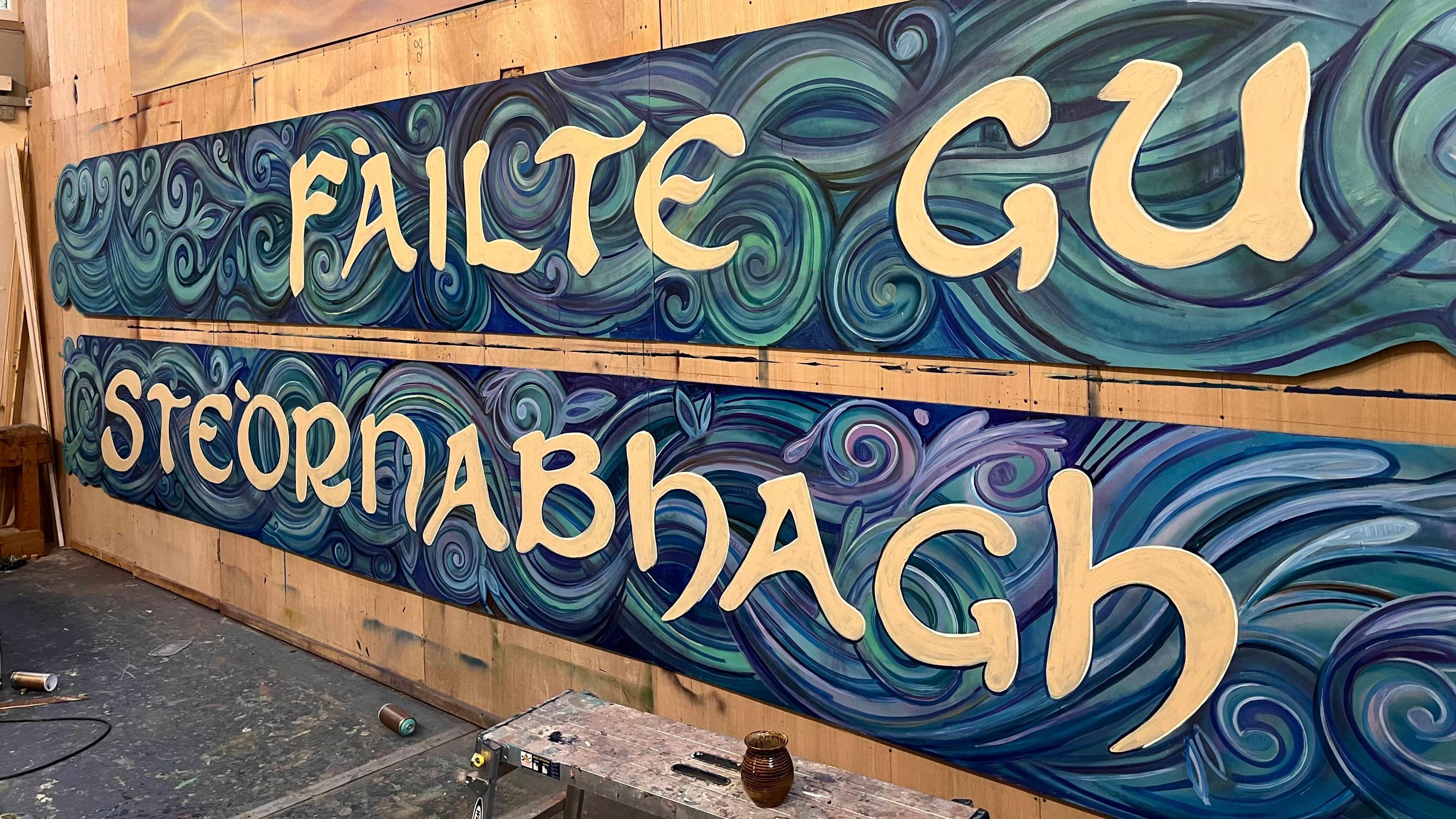 Ìomhaigh den dealbh-bhalla san stiùidio de na bùird a tha ag ràdh 'Fàilte gu Steòrnabhagh' ann an sgrìobhadh gheal le dathan gorm sa chùlaibh.
