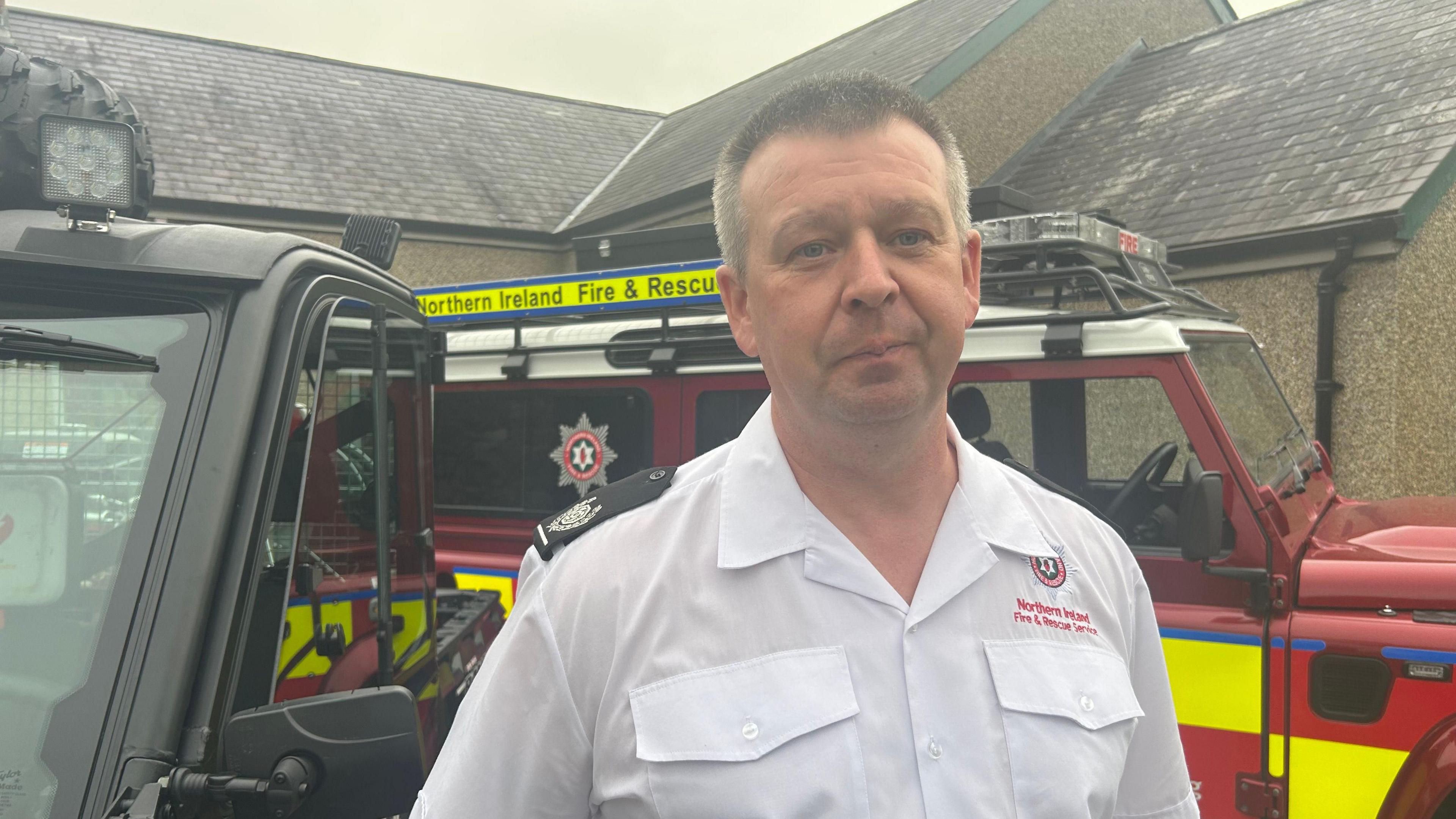 A man in a white shirt stands in front of two emergency response vehicles