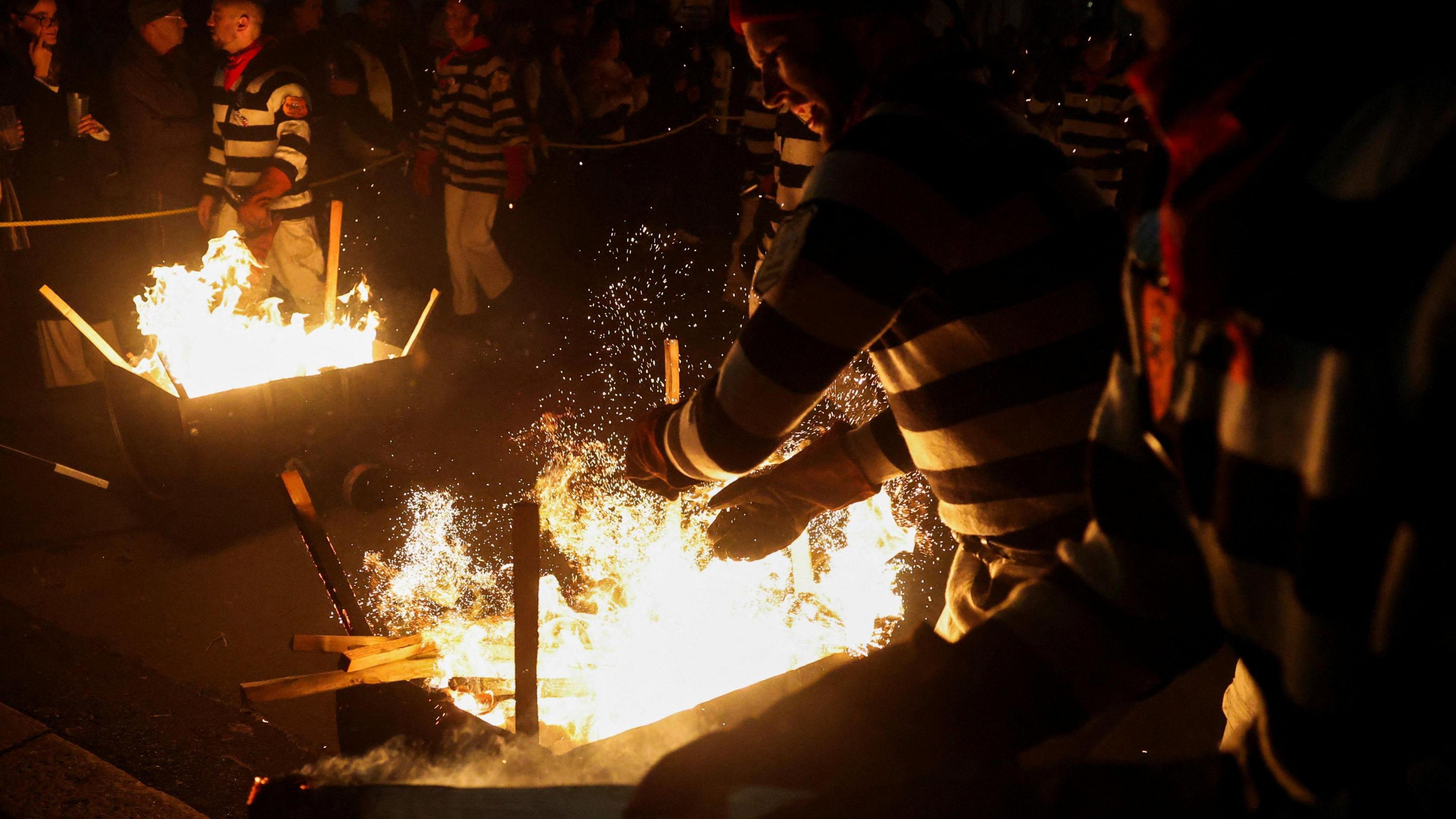 Members of a bonfire society in Lewes, wearing blue and white hooped jerseys. light their torches from an open fire.