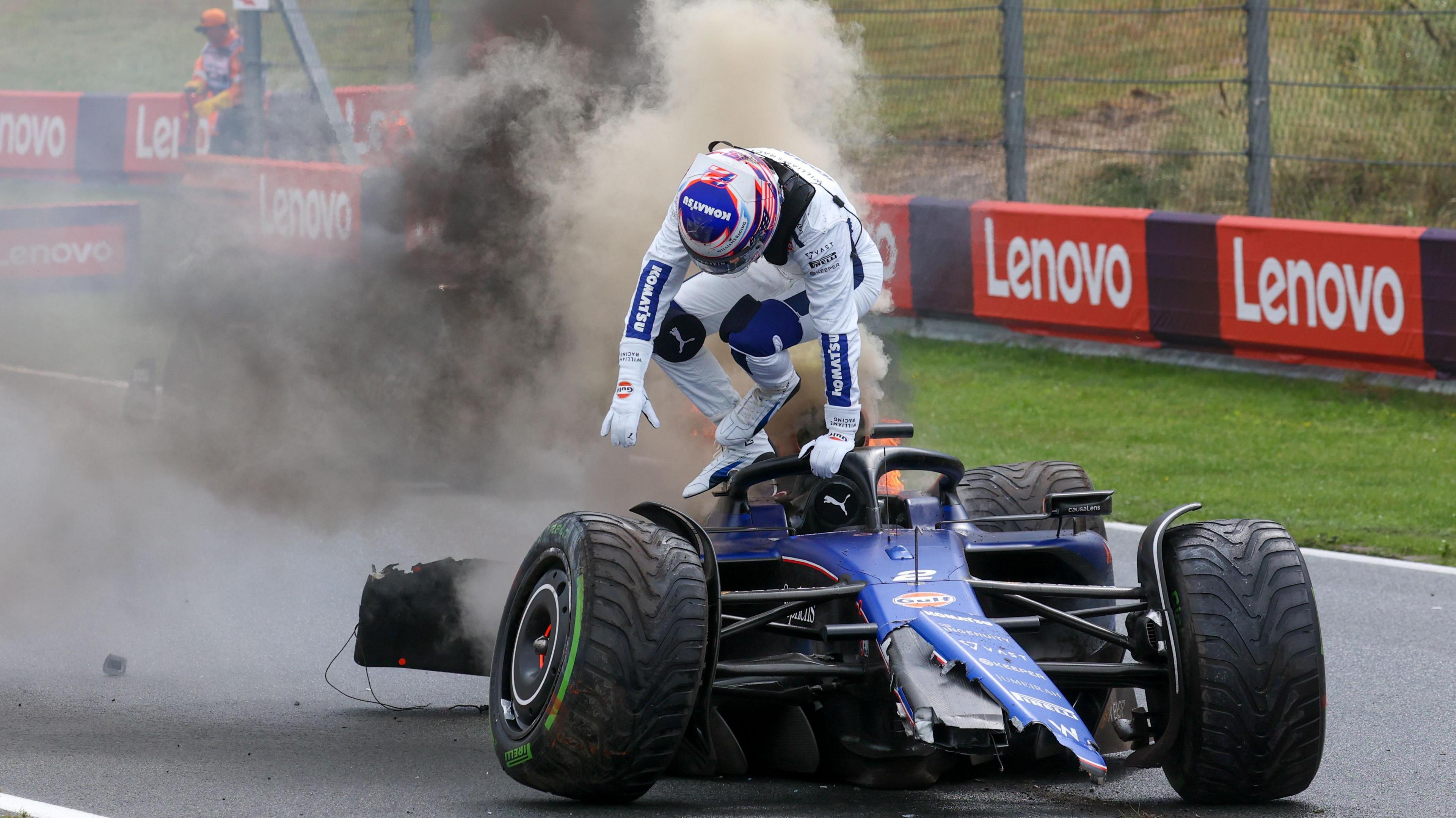 Logan Sargeant climbs out of his badly damaged Williams, which has lost its rear wing and has fie and smoke coming out of the rear, after crashing during practice for the Dutch Grand Prix