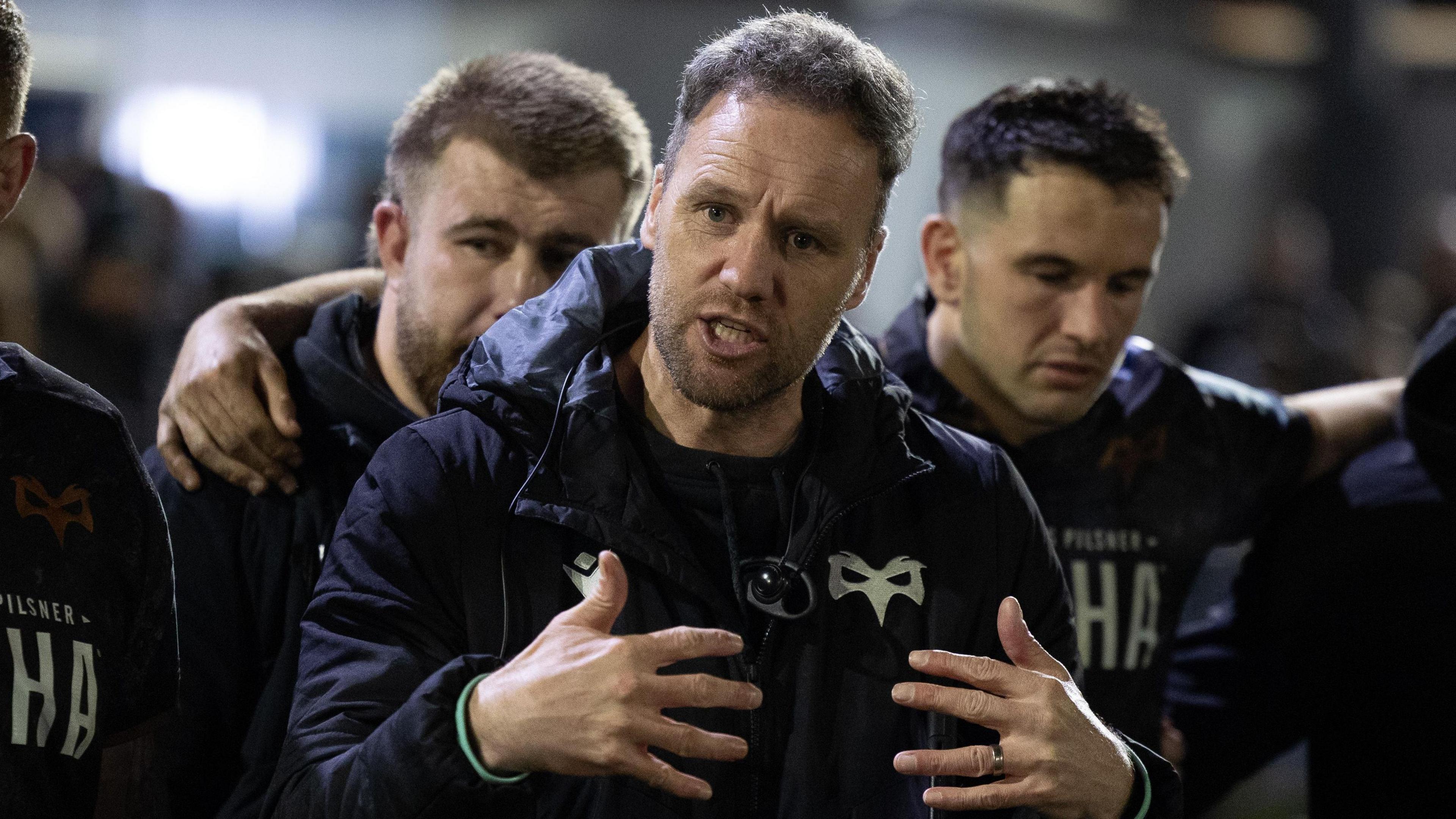 Ospreys head coach Mark Jones gestures with his hands as he talks to his squad in a huddle