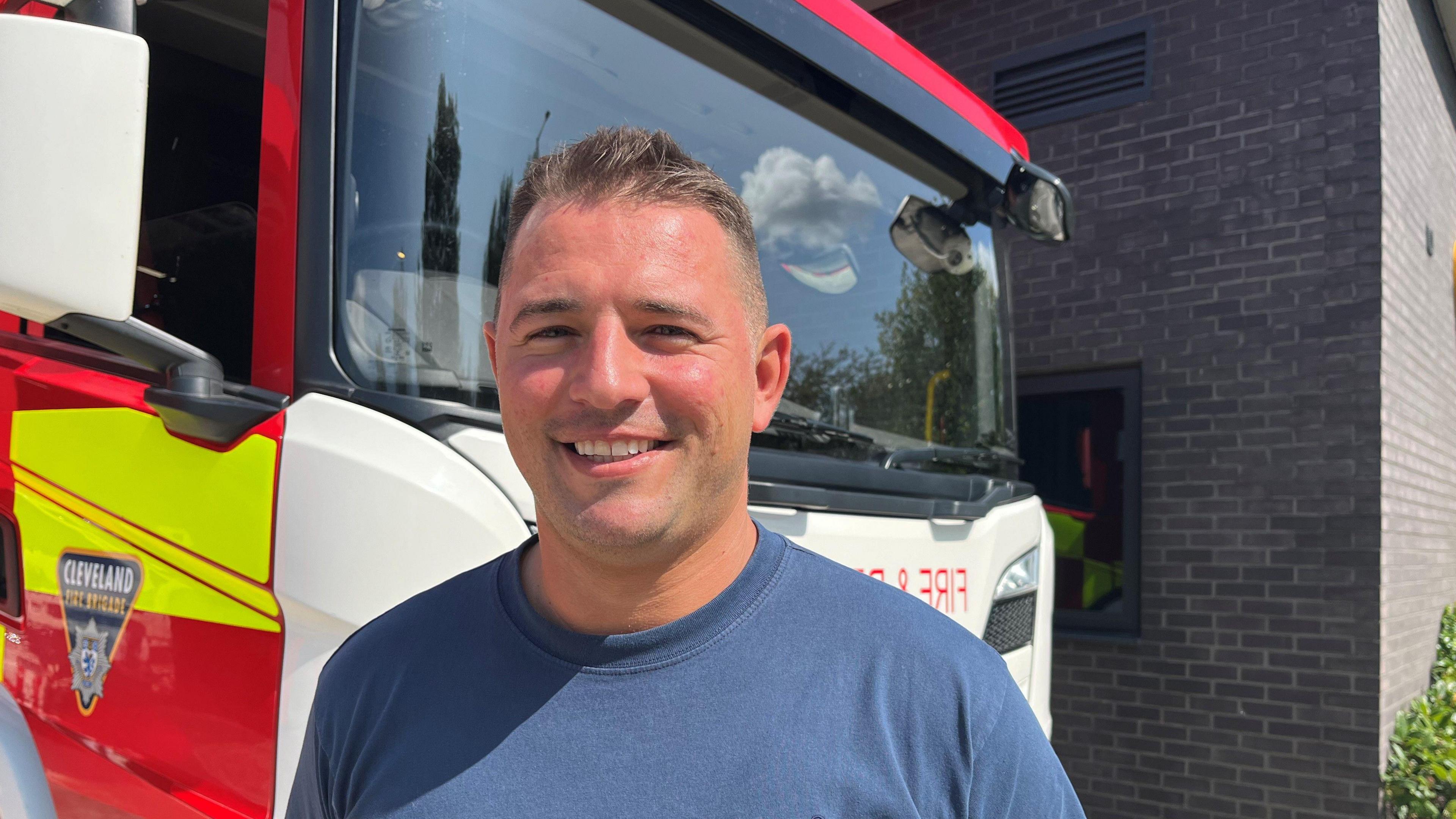 A man with dark grey hair stood in front of fire engine.