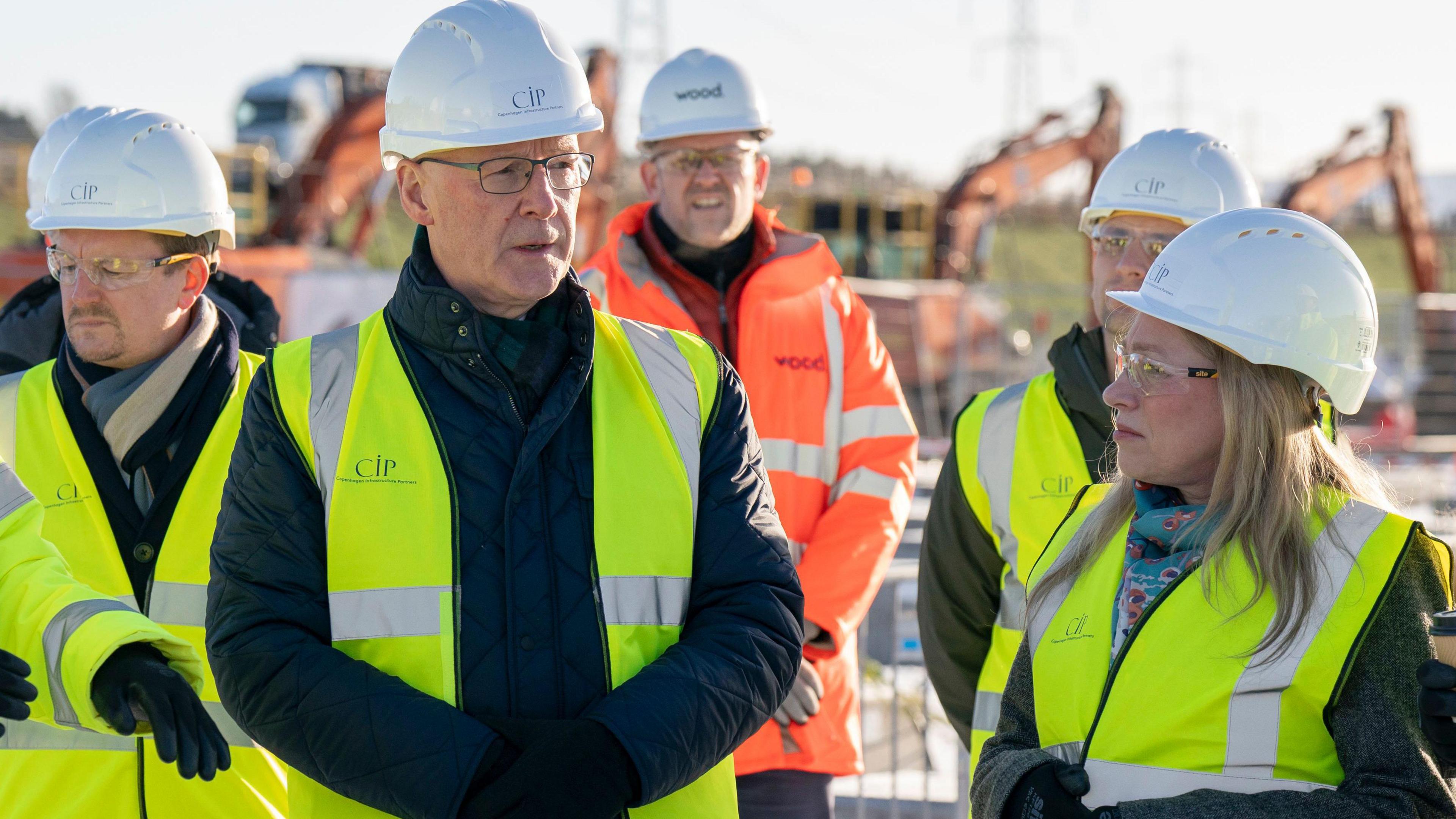 John Swinney wearing a yellow high-vis jacket and white hard hat with several similarly dressed members of the CIP team on the construction site at Coalburn 1