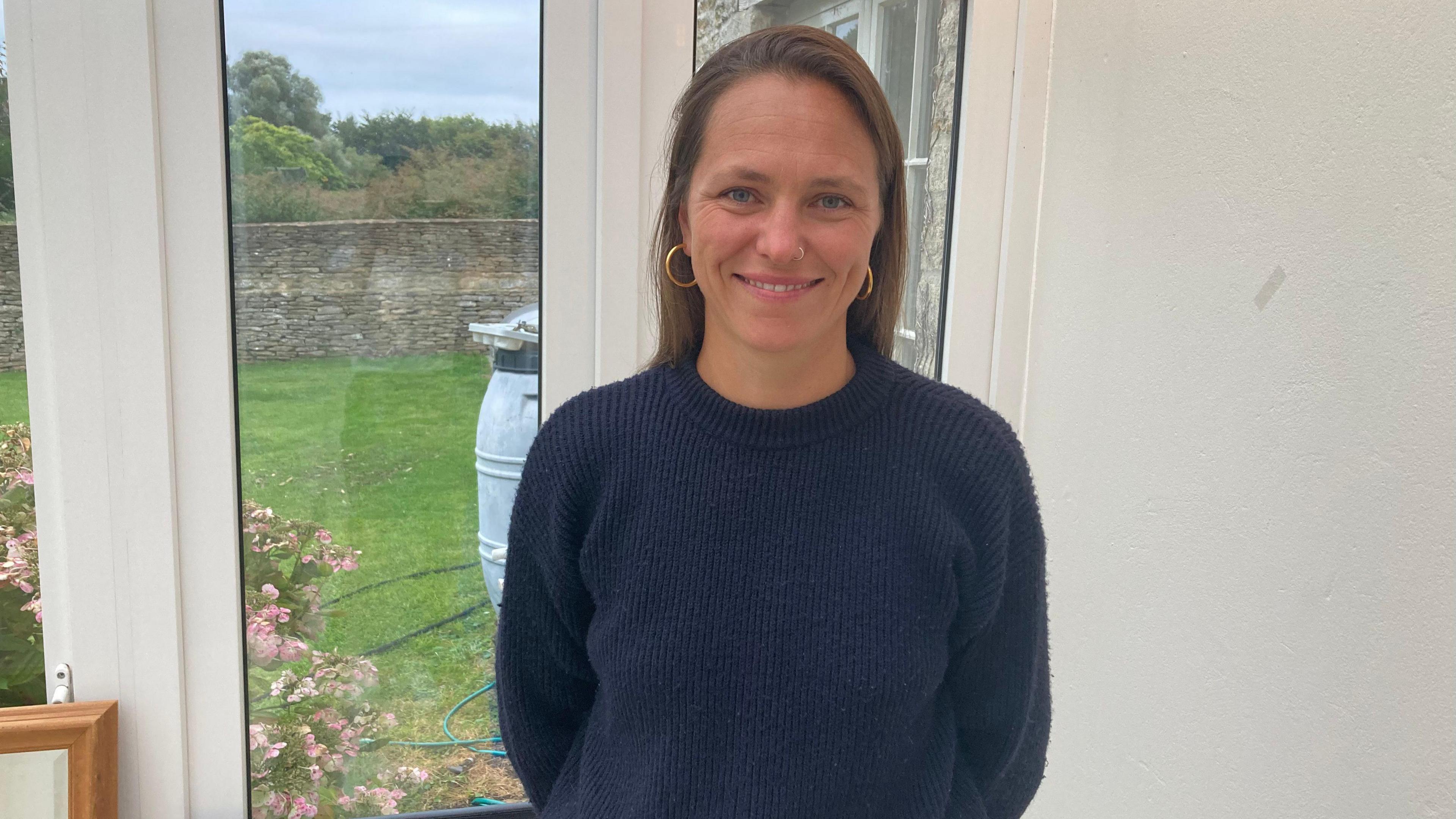 Anna standing in a navy jumper in front of double glass doors 