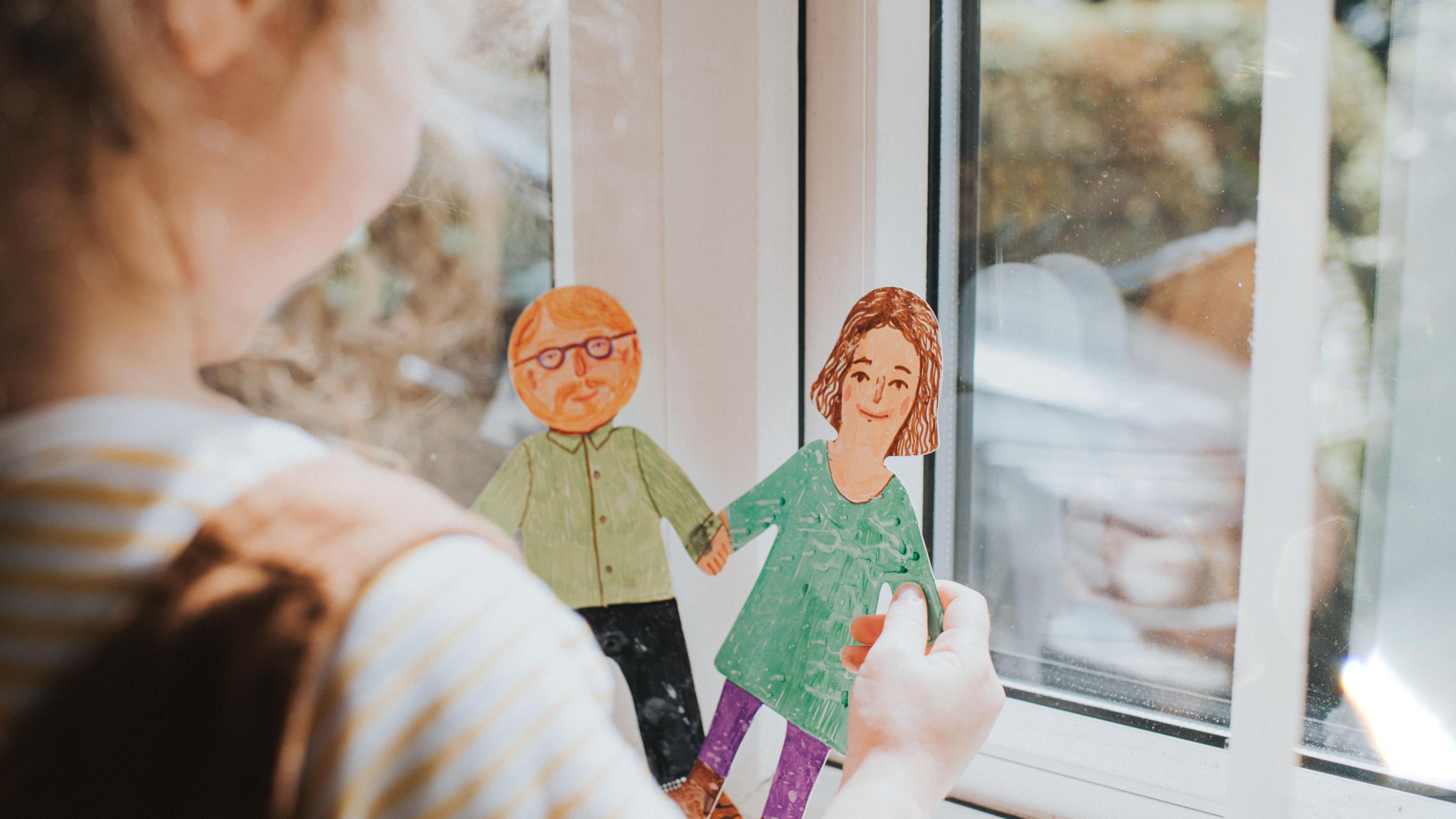 A small child holds a paper cut out of a couple holding hands.