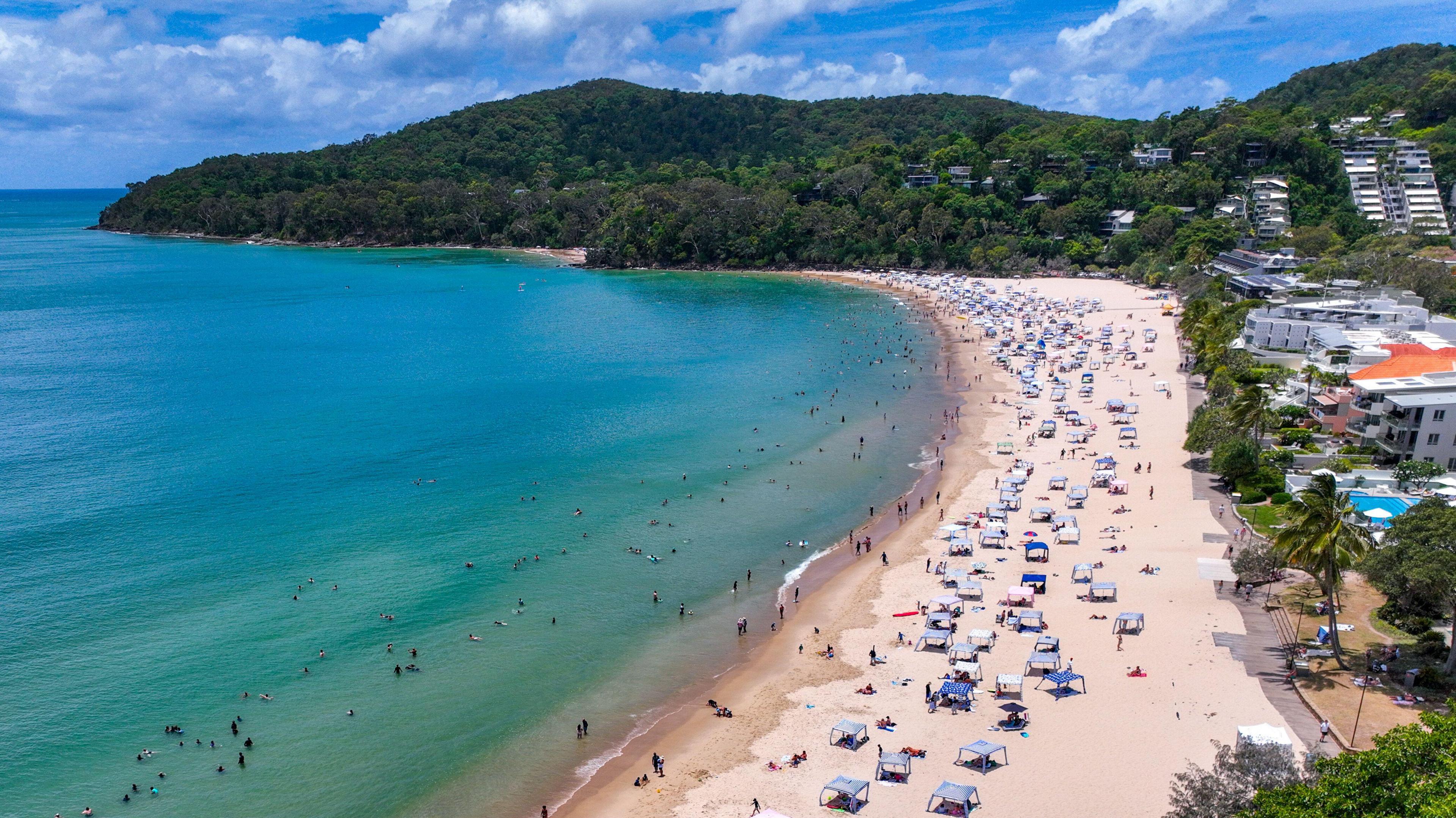 A drone shot of Main Beach in Noosa showing cabanas on the sand and swimmers in the water along the whole length of the beach