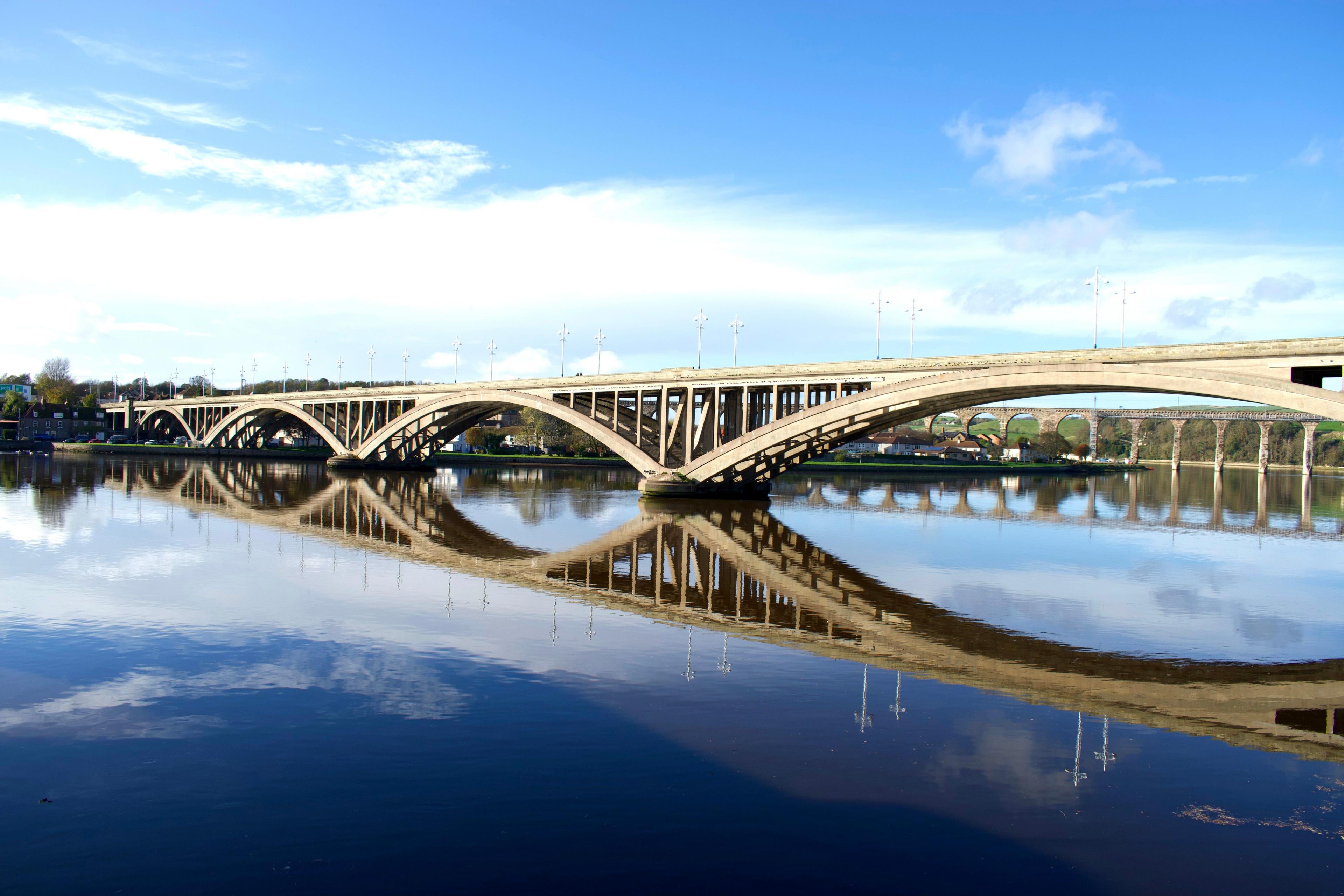 The arches of a bridge and viaduct are reflected in the River Tweed