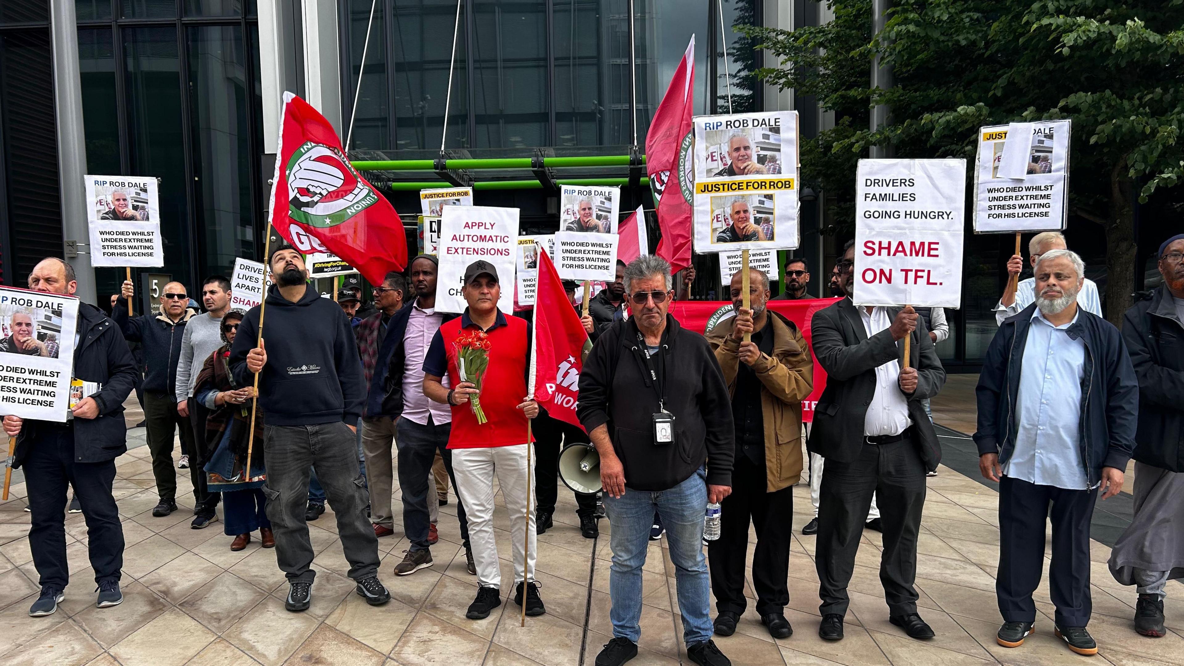 The protestors stand in a line holding up banners and pickets